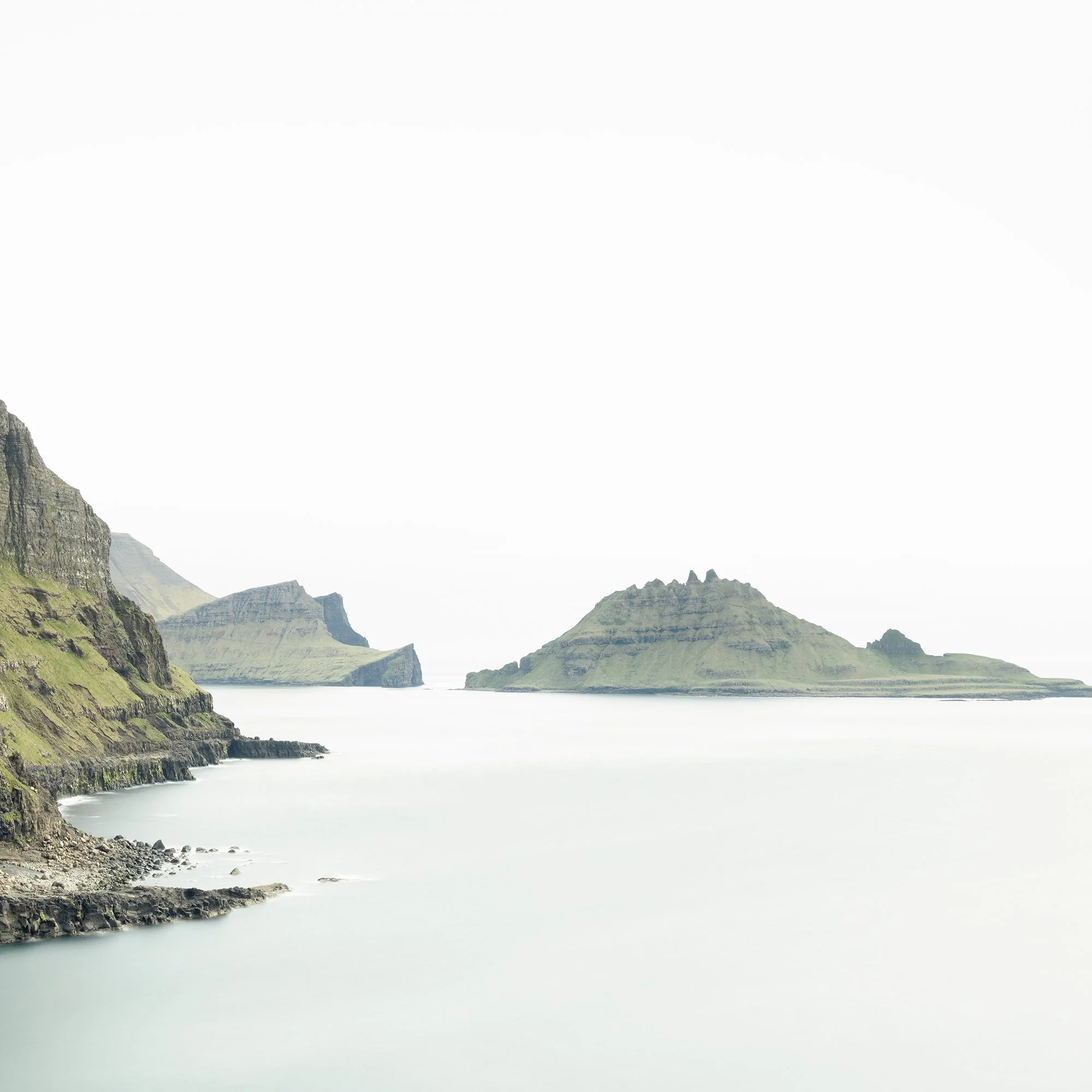 Gerald Berghammer - Color Photography. Cliffs and green hills along a body of water, with distant islands or landmasses in the background under a cloudy sky. Print detail 2