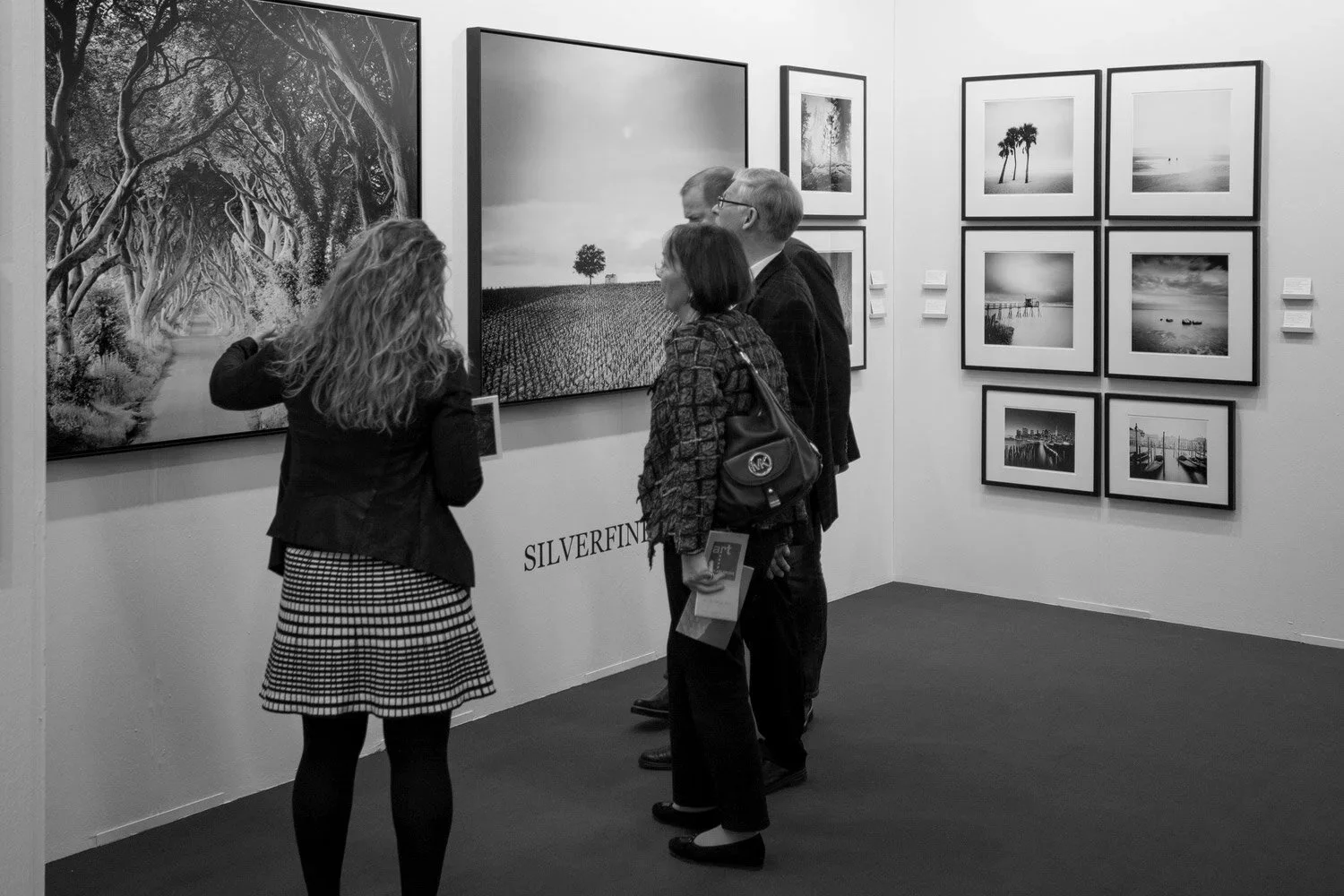 Visitors in conversation at the Galerie Edition Camos stand with fine art photography by Gerald Berghammer on display, art KARLSRUHE 2017.