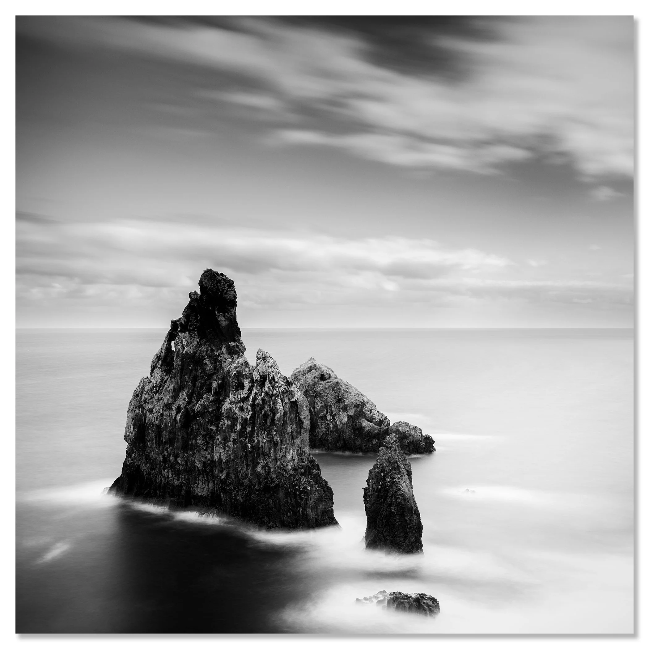 Three large rocks rising from the sea close to the shore under an overcast sky – dibond frameless