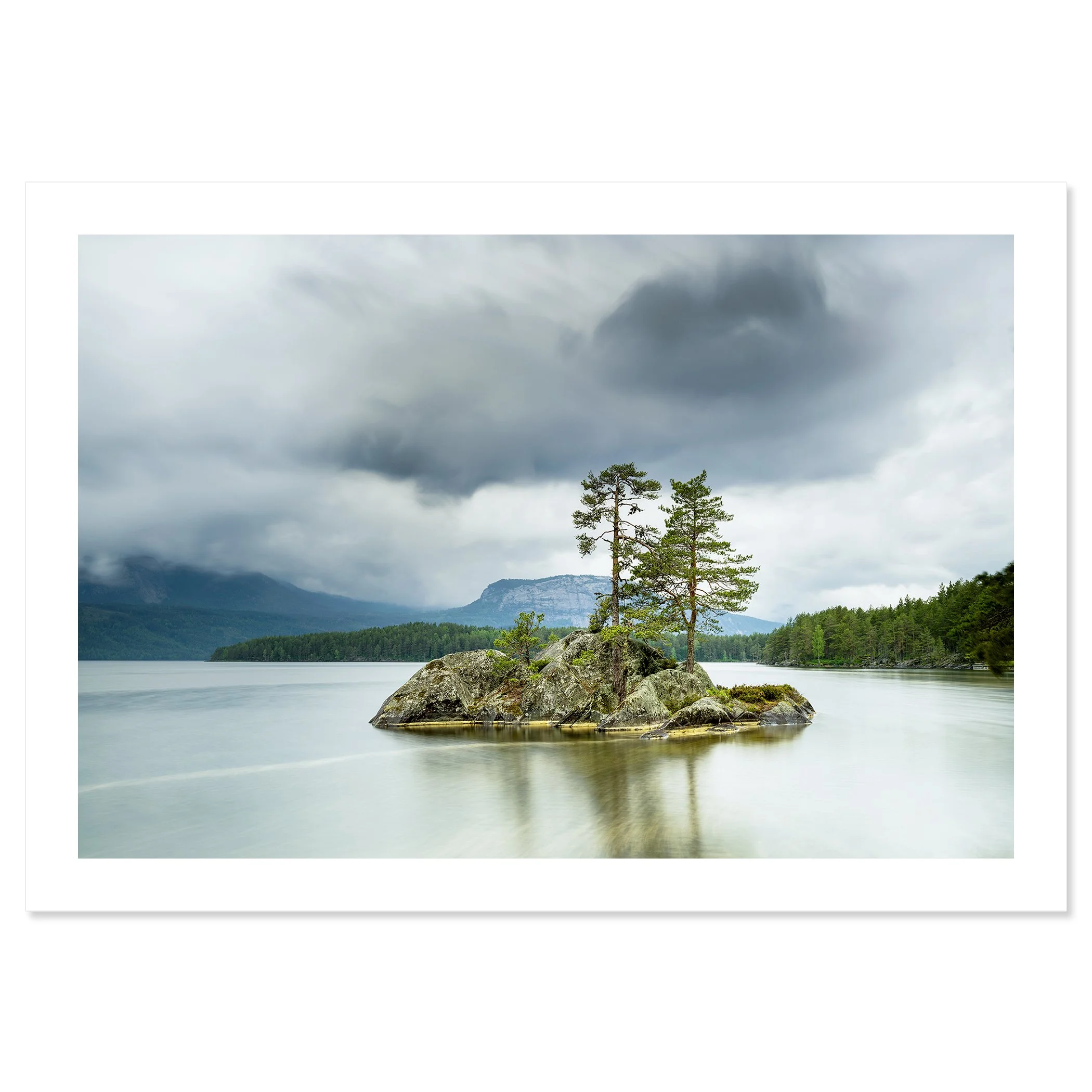 Gerald Berghammer - Color Photography. A small rocky island with tall pine trees surrounded by a calm lake under a cloudy sky and mountains behind. Fine art print only
