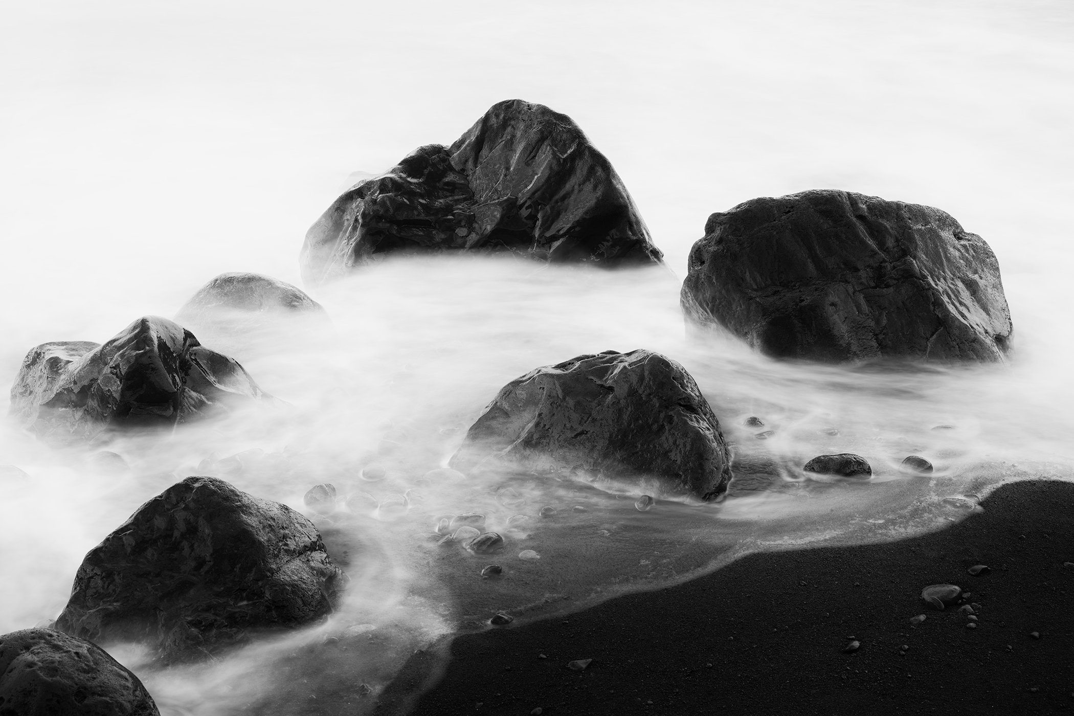 Monochrome fine art photograph of ocean rocks and misty water on a dramatic shoreline, photo by Gerald Berghammer.