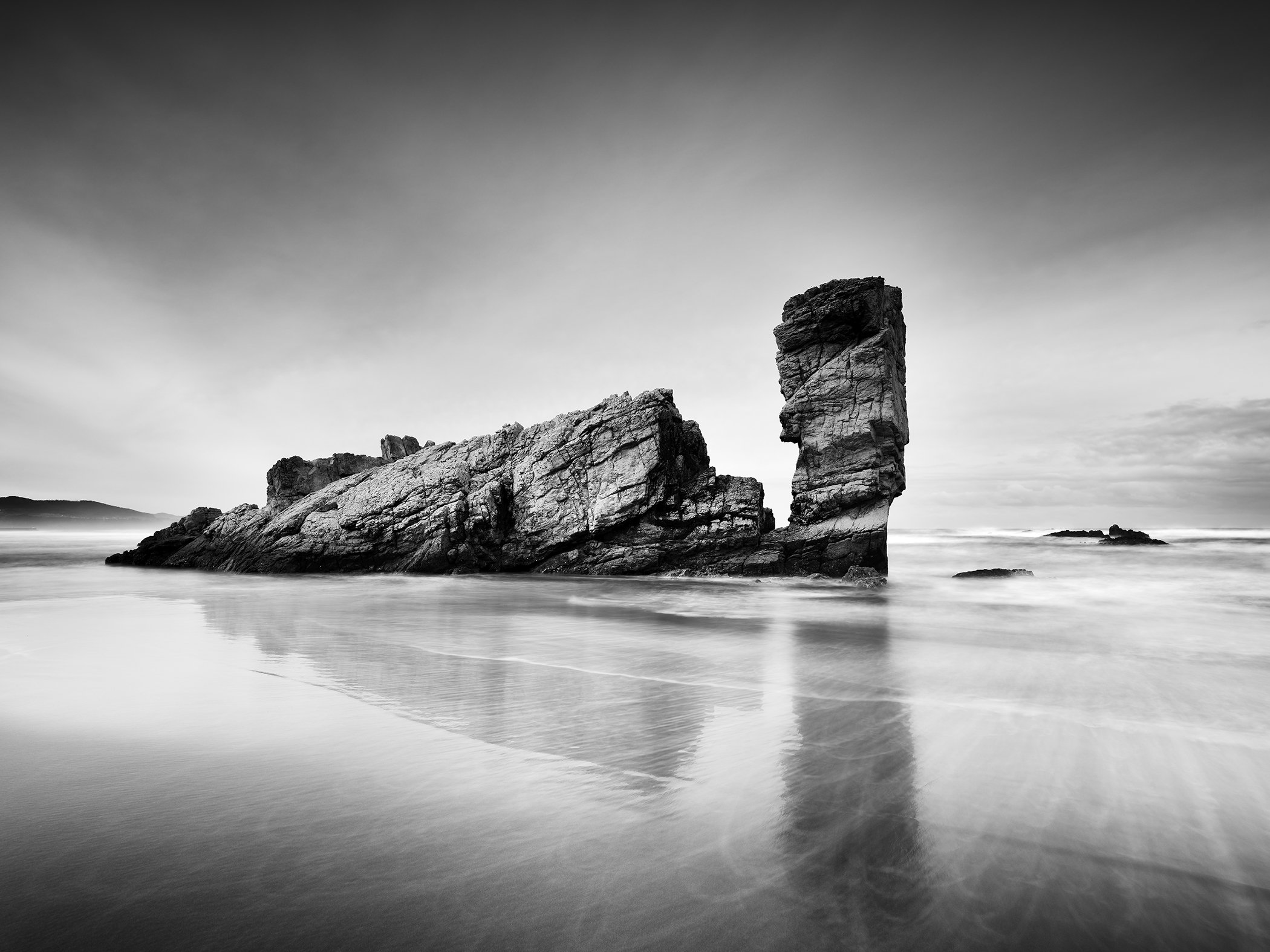 Black-and-white beach landscape with rugged rock formation and reflection in wet sand