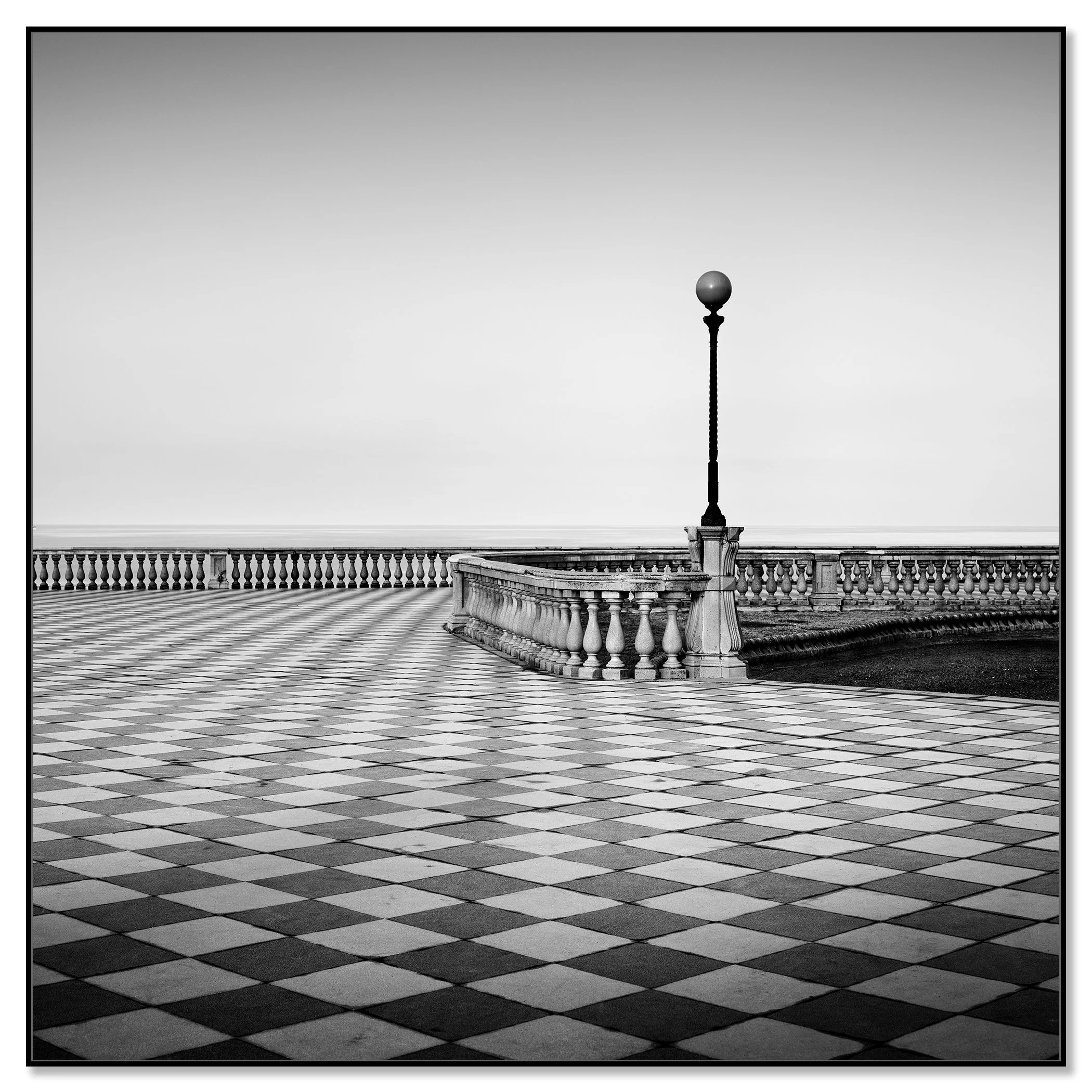 Black and white photo of an empty seaside promenade with chequerboard tiles, railings and a single lamppost – framed ArtBox black