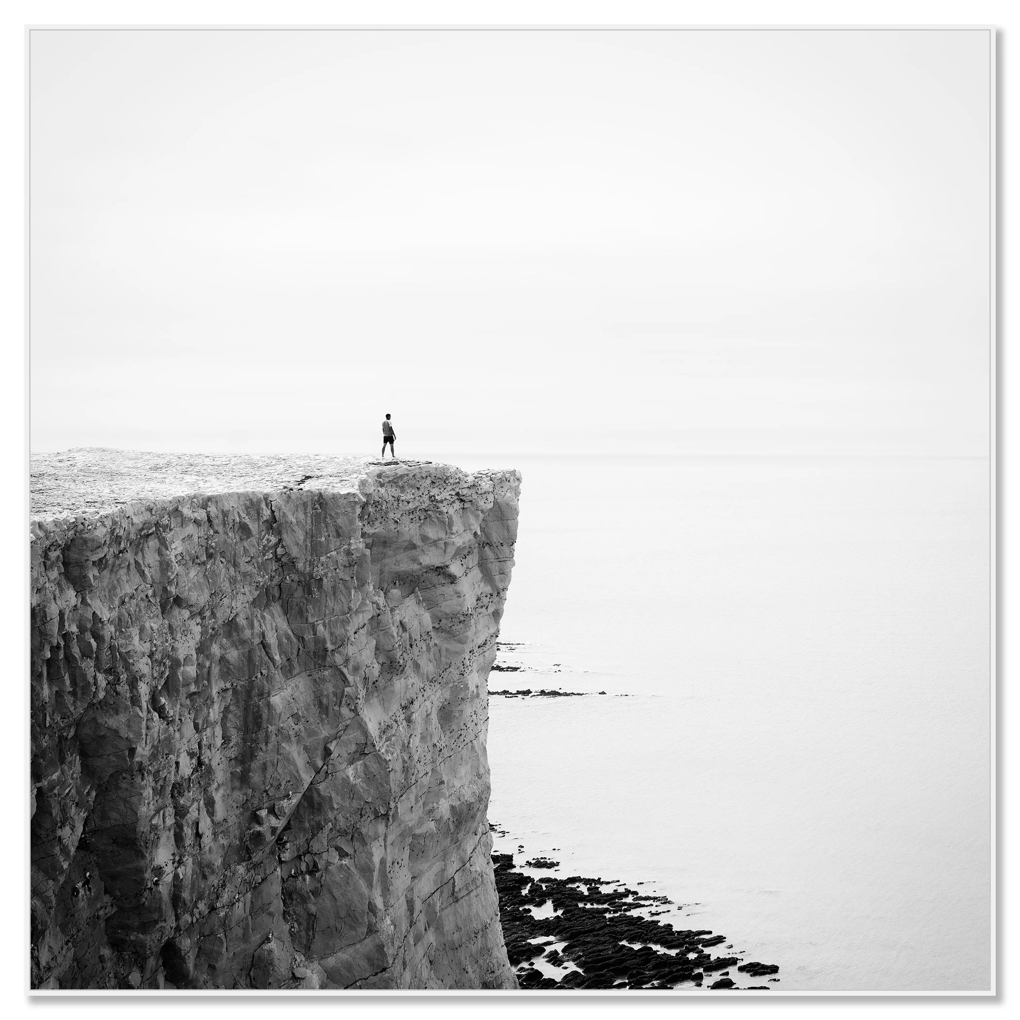 Person standing alone on a white cliff edge overlooking the England coast and ocean – framed ArtBox white