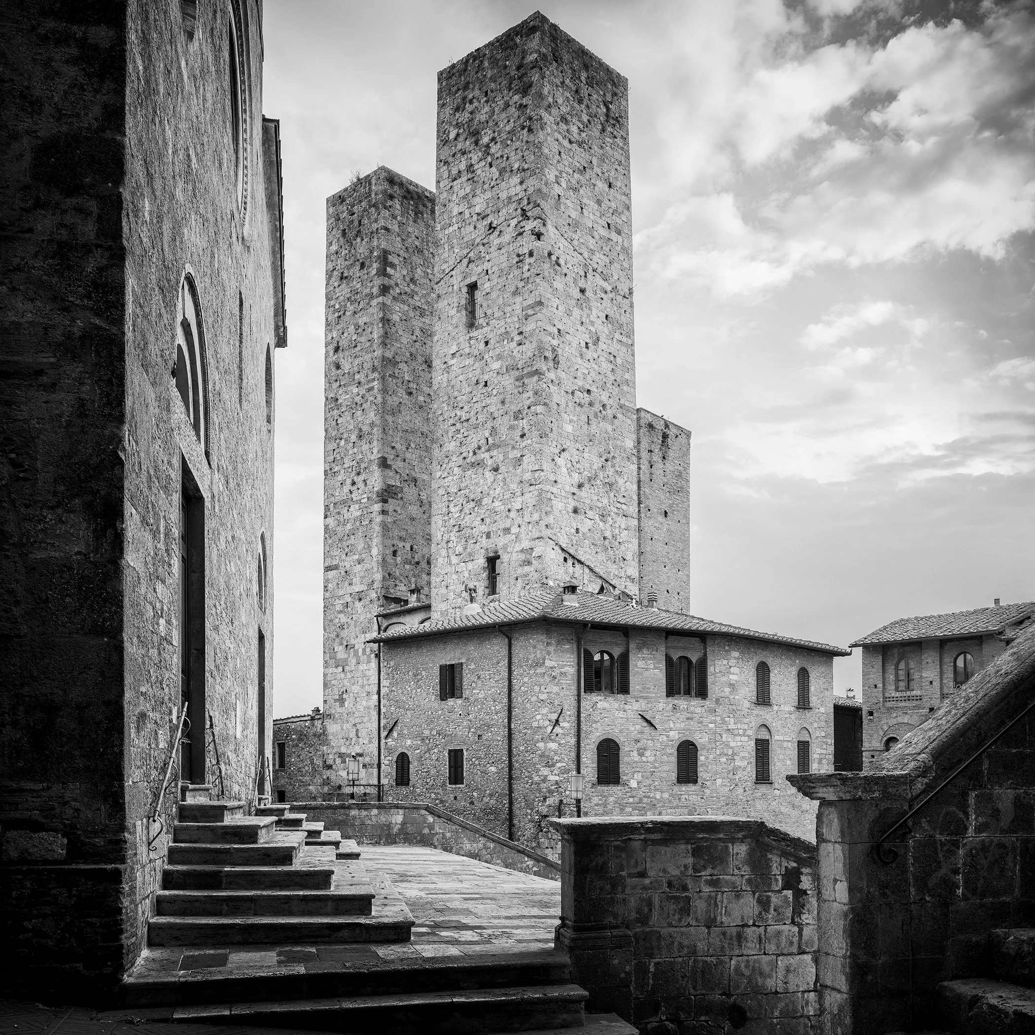 Monochrome photograph of medieval towers and old stone buildings in San Gimignano under a cloudy sky