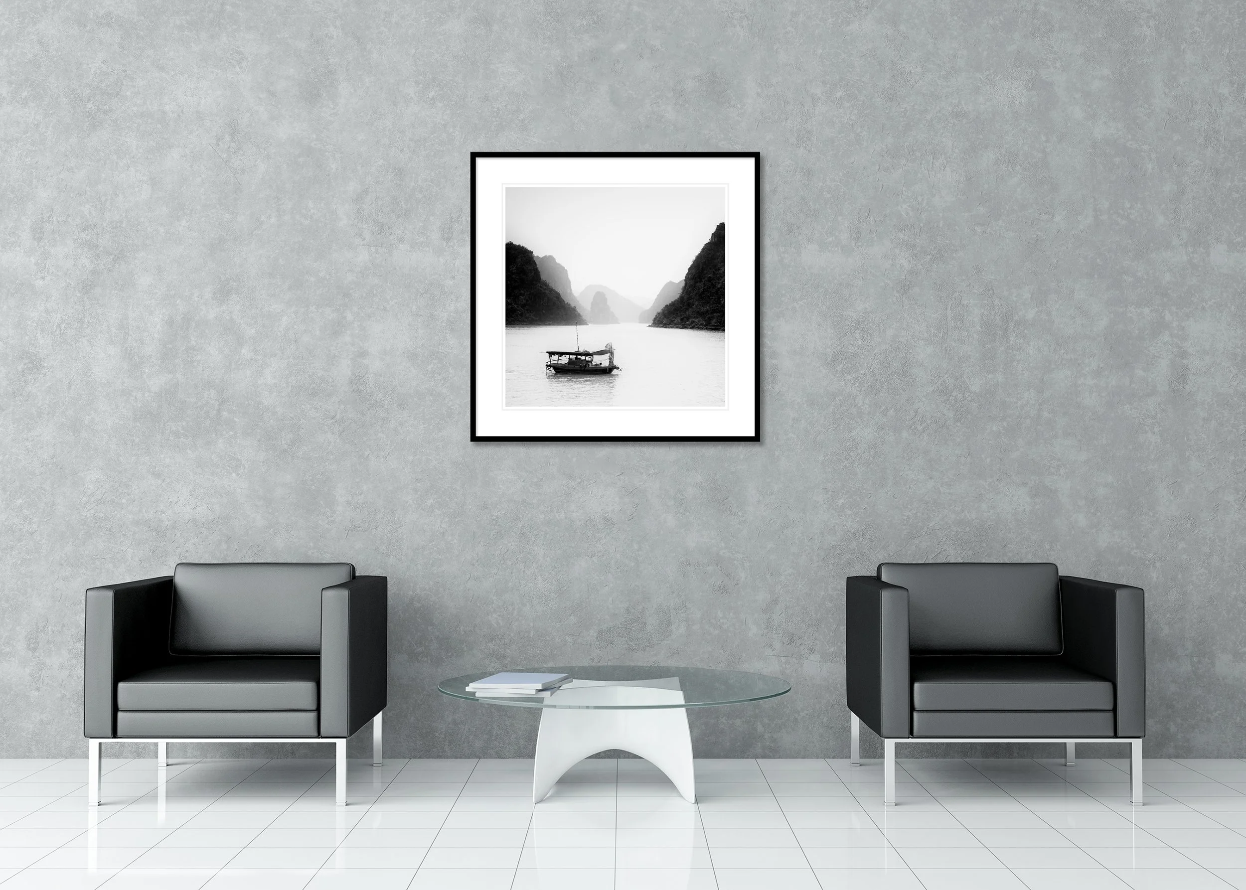 Black and white photograph of a small boat floating on calm water between misty limestone mountains. Archival Pigment Print – Classic Frame with Passe-Partout