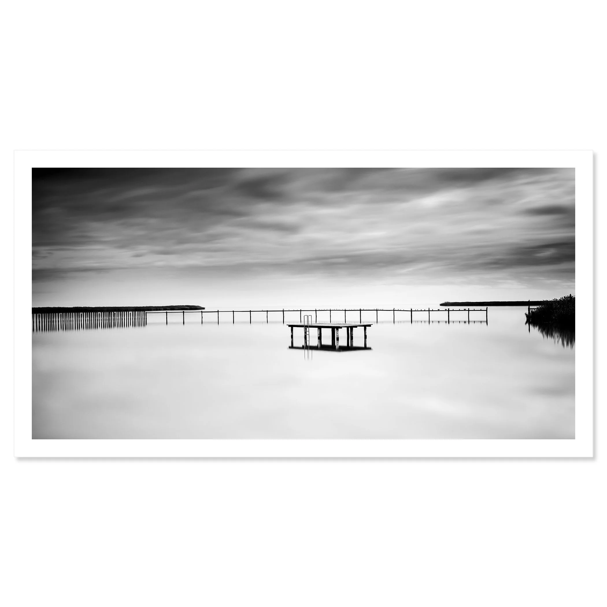 © 2023 Gerald Berghammer - Black and white minimalist waterscape. A calm body of water with a floating dock and a pier in the background, under a cloudy sky. Fine art print only