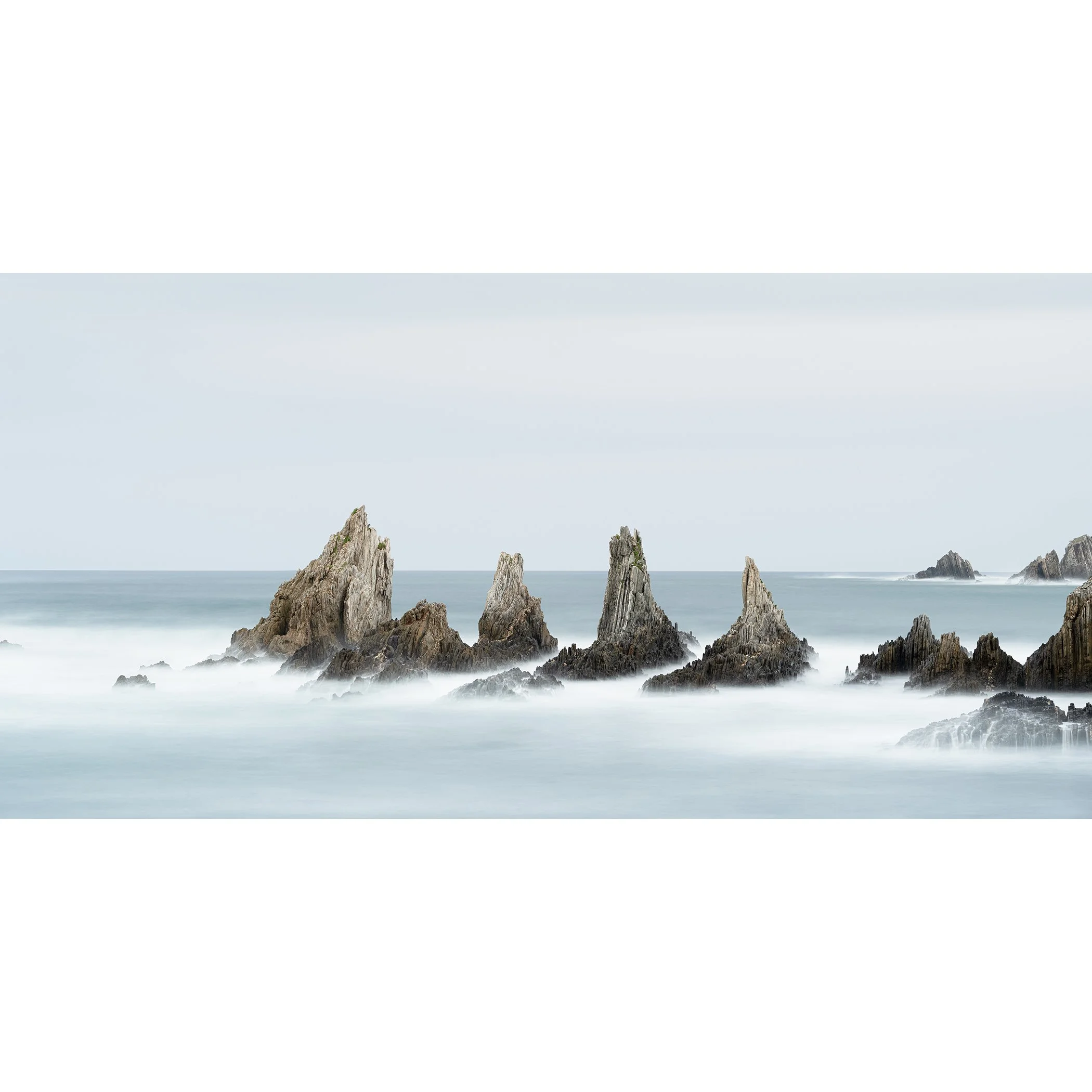 Gerald Bergammer - Color minimalist seascape photography. Long exposure photo of jagged rocks in the ocean with misty water and a cloudy sky.