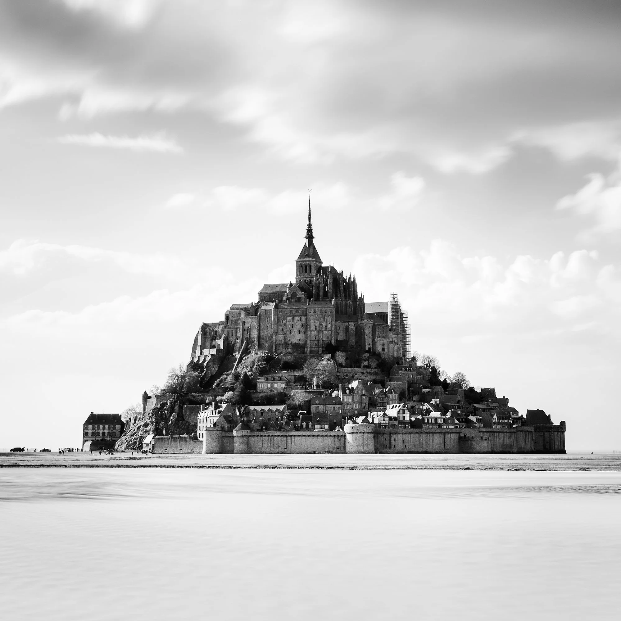 © 2023 Gerald Berghammer - B&W photography. Mont Saint-Michel, a historic island with a tall spire and medieval architecture, surrounded by water and clouds. Print detail 3