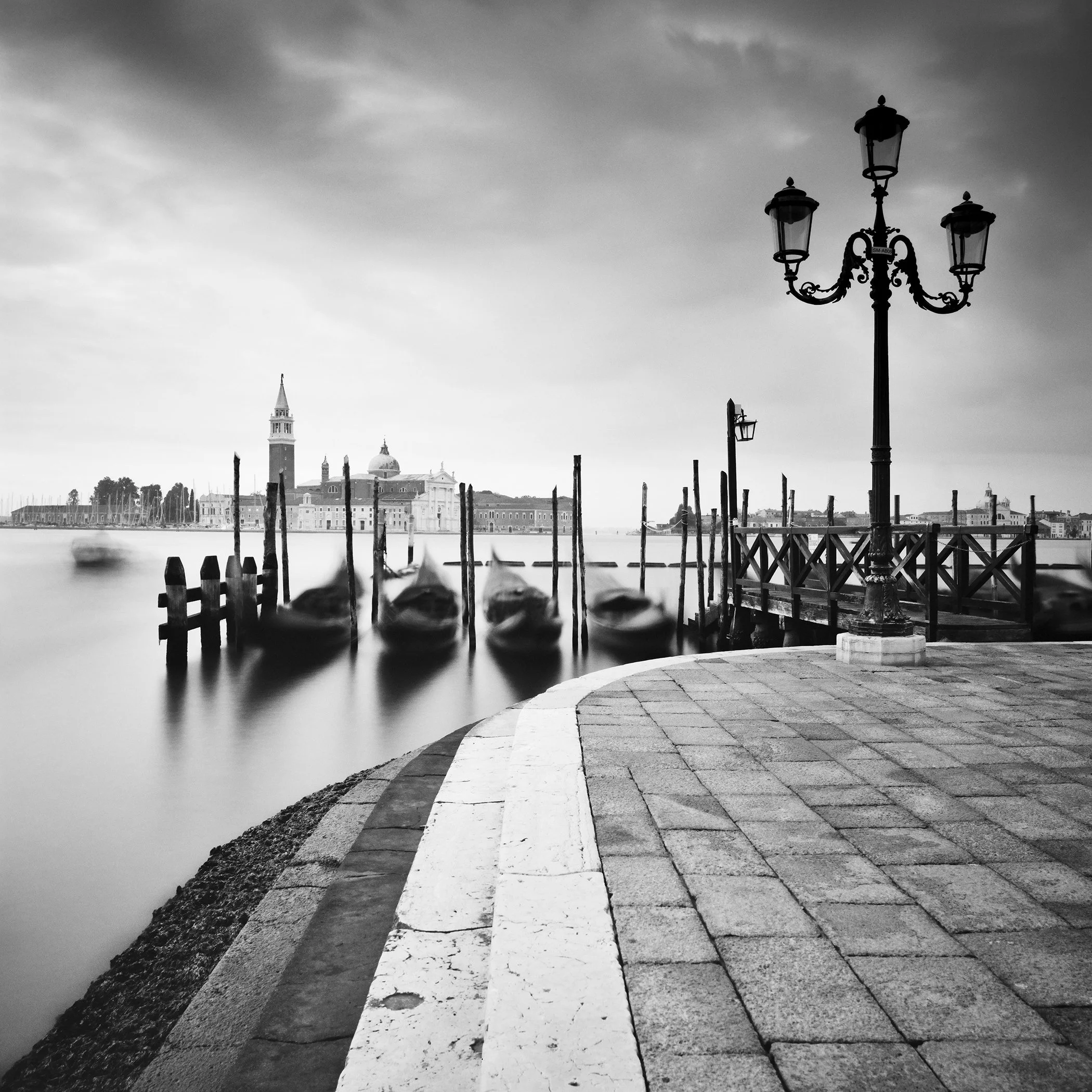 Moody monochrome Venice photograph with blurred gondolas, San Giorgio Maggiore and ornate lamp post by Gerald Berghammer