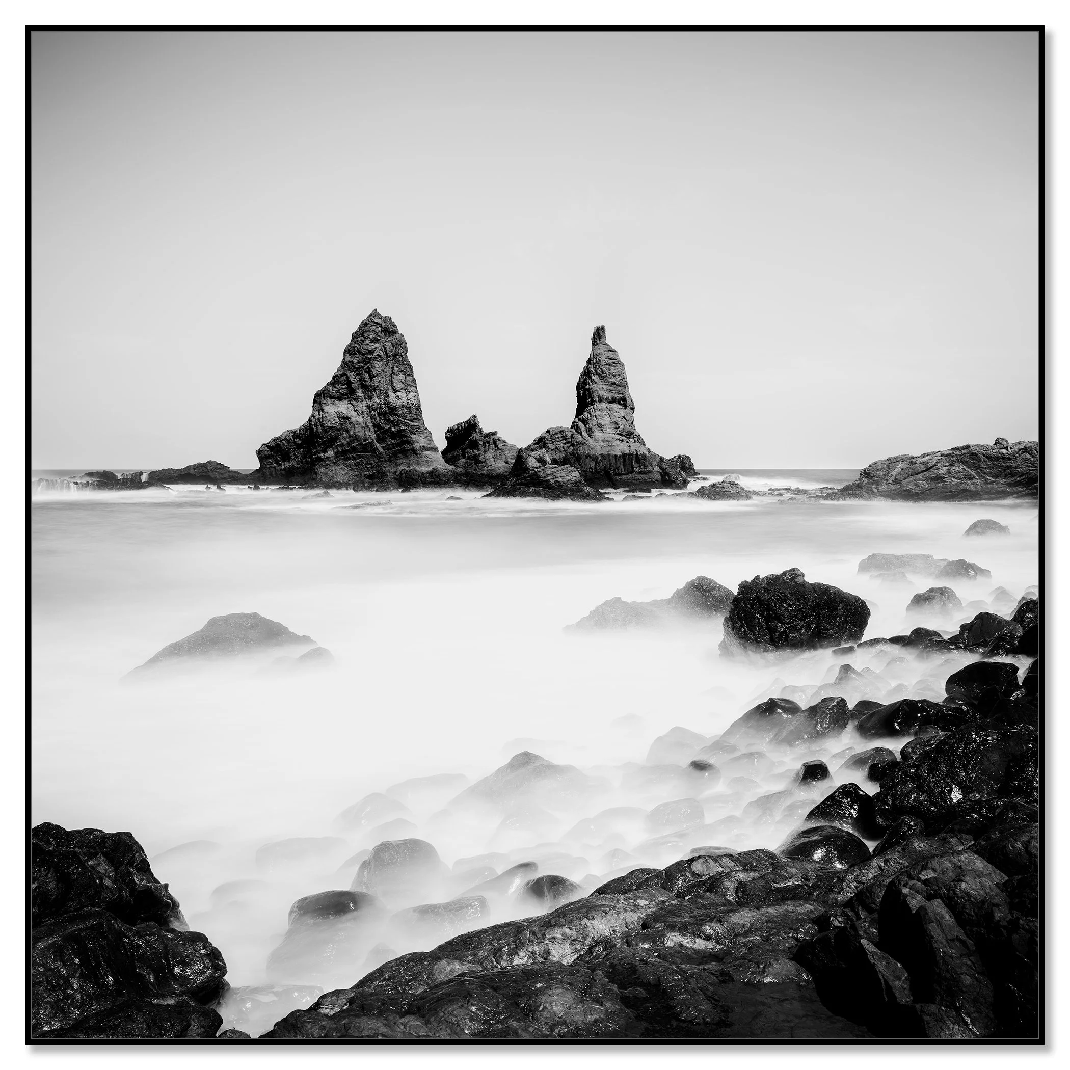 Moody monochrome seascape with rugged rock formations, smooth ocean water and a rocky foreground – framed ArtBox black