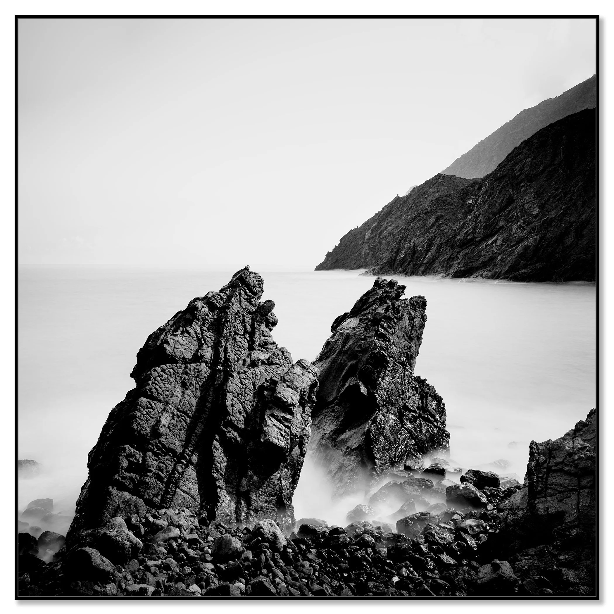 Black and white Atlantic seascape: rocky shoreline, large sea boulders, and mountains in the distance – framed ArtBox black