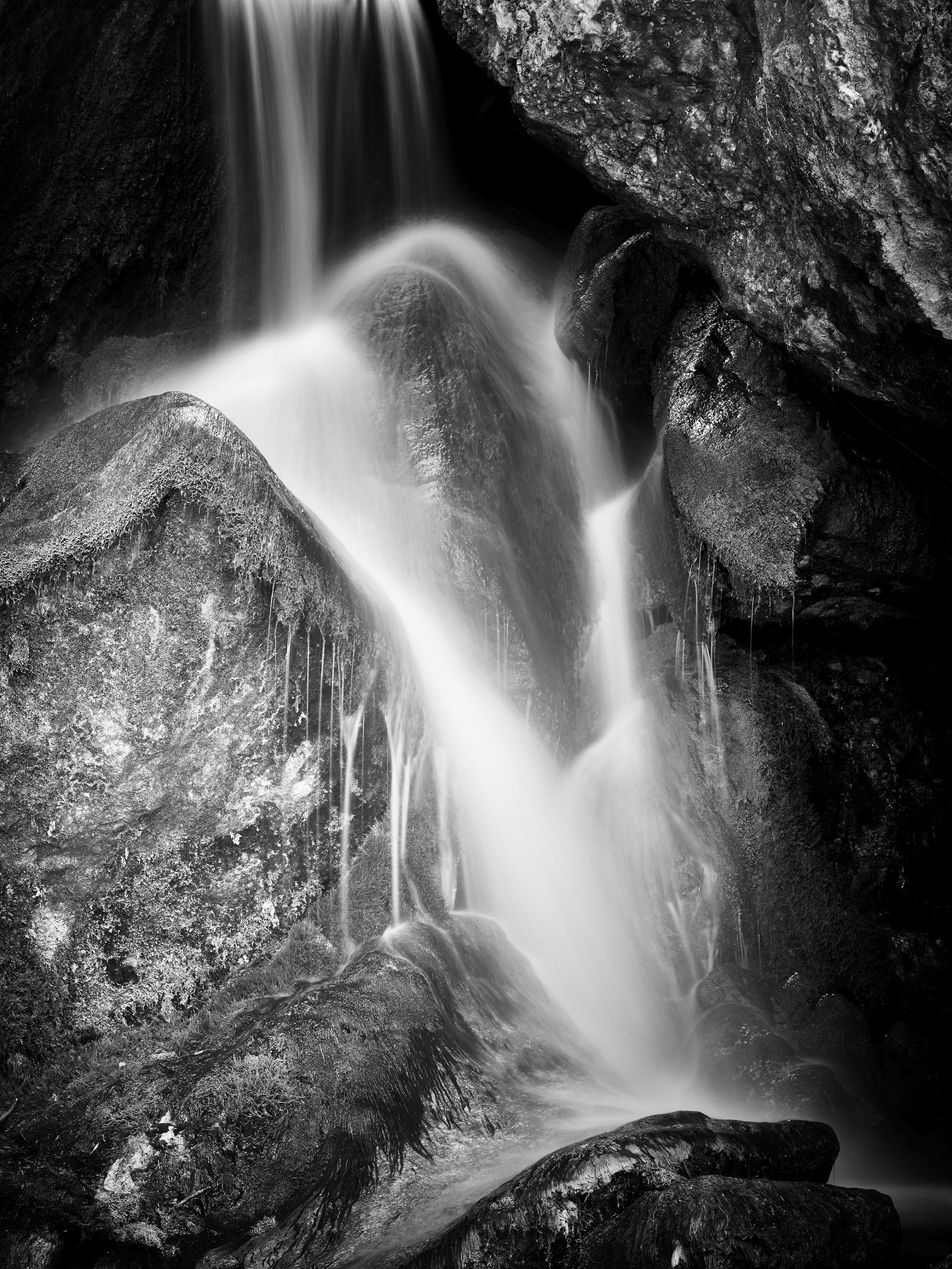 Black-and-white long-exposure photograph of a waterfall flowing between rugged rocks in Austria. Photo by Gerald Berghammer.