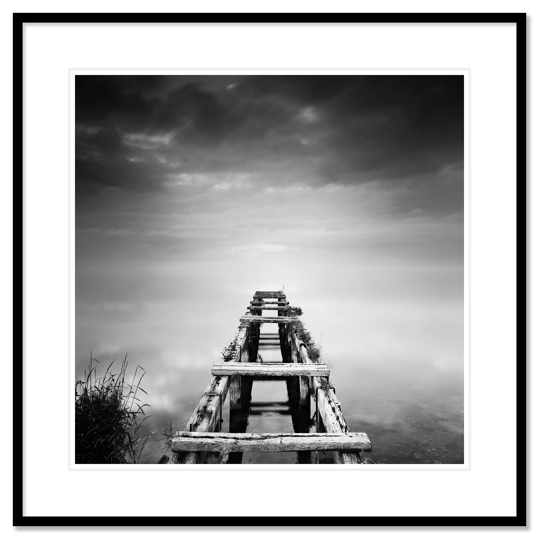 Gerald Berghammer - Black and white waterscape photography. An old abandoned wooden dock extending into a calm body of water under a cloudy sky. Classic framed black