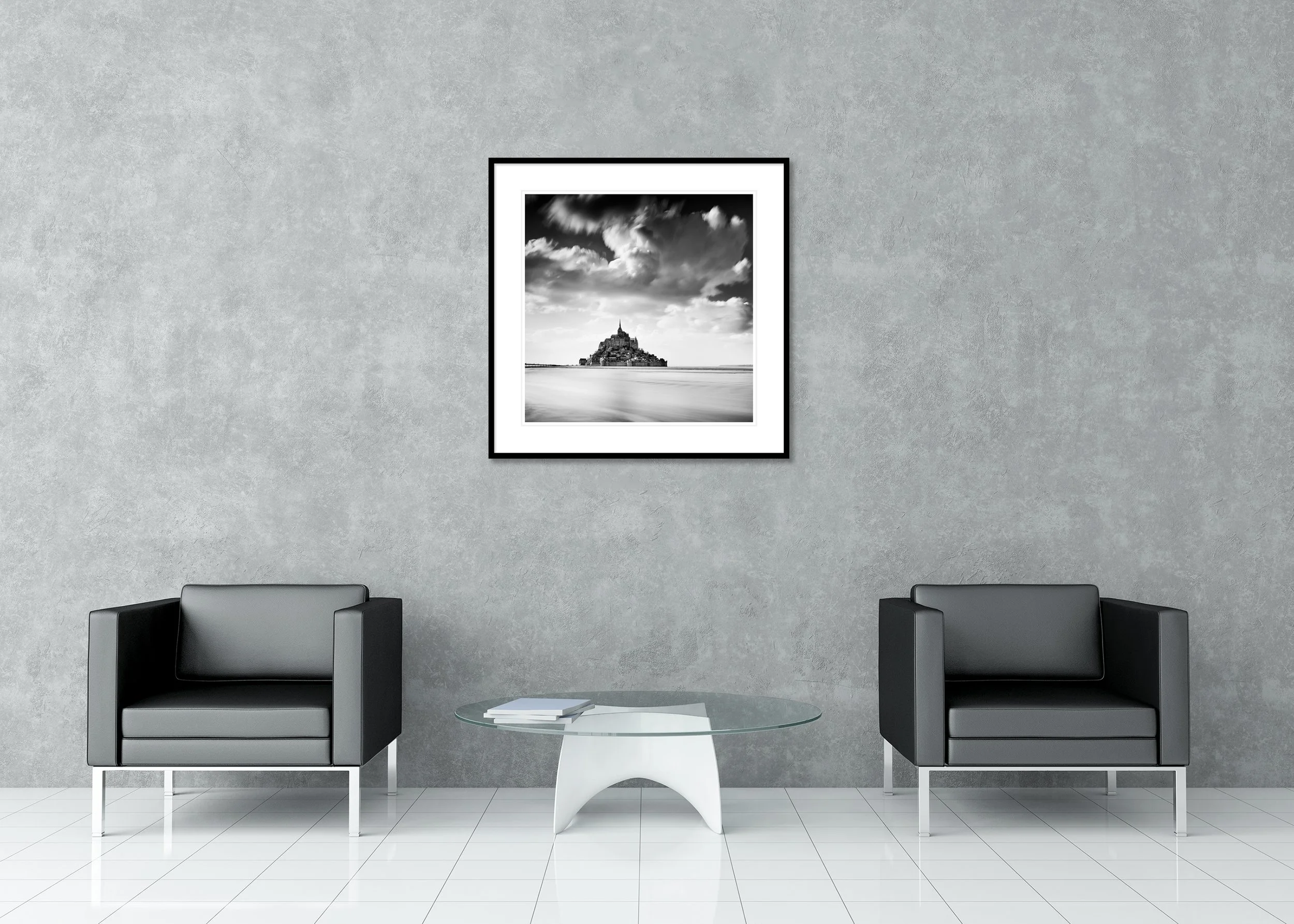 Monochrome archival pigment print of Mont Saint-Michel in France in a classic frame with a mount, above tidal water under a vast cloudy sky.