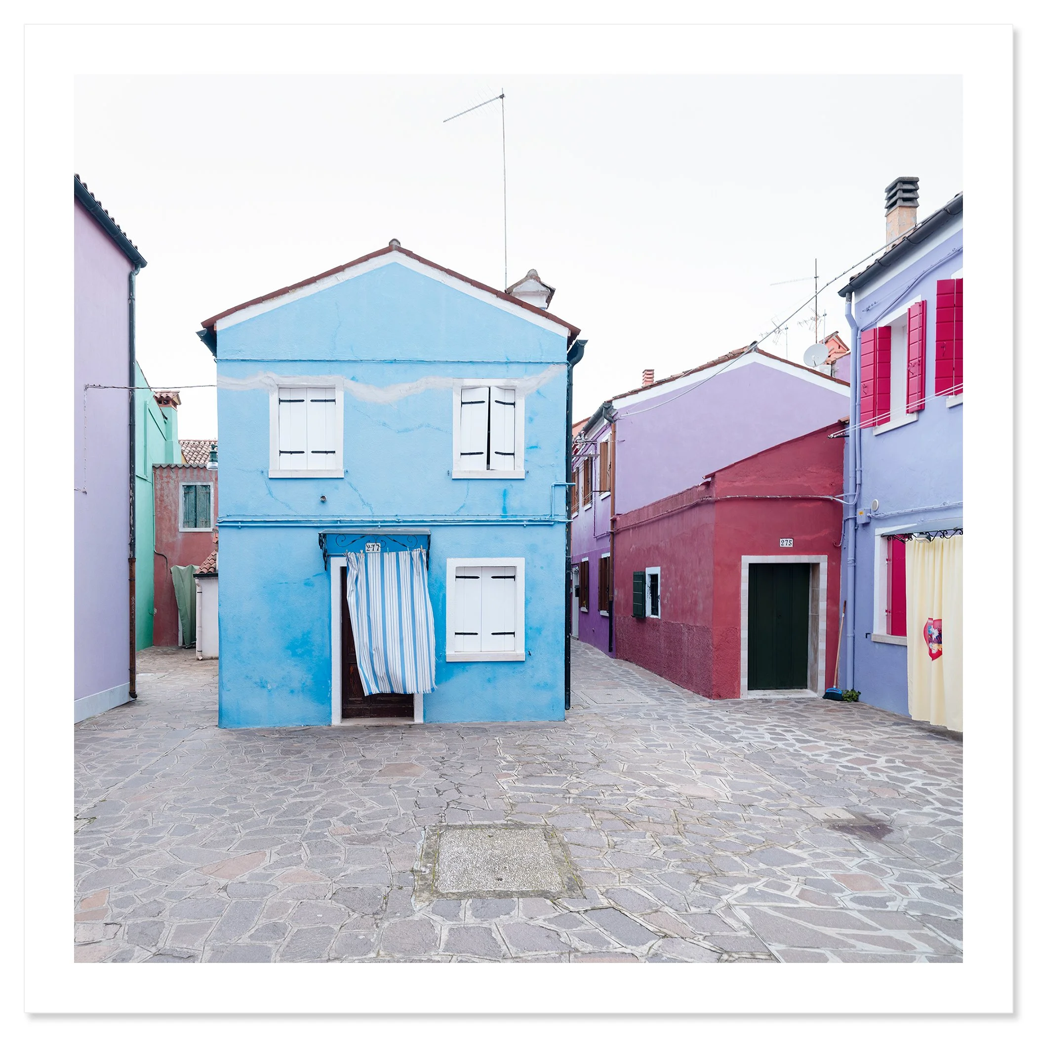 © 2025 Gerald Berghammer photo - Colorful houses in pastel shades on a cobblestone street, with colorful windows and a striped curtain hanging in front of one house. Fine art print only