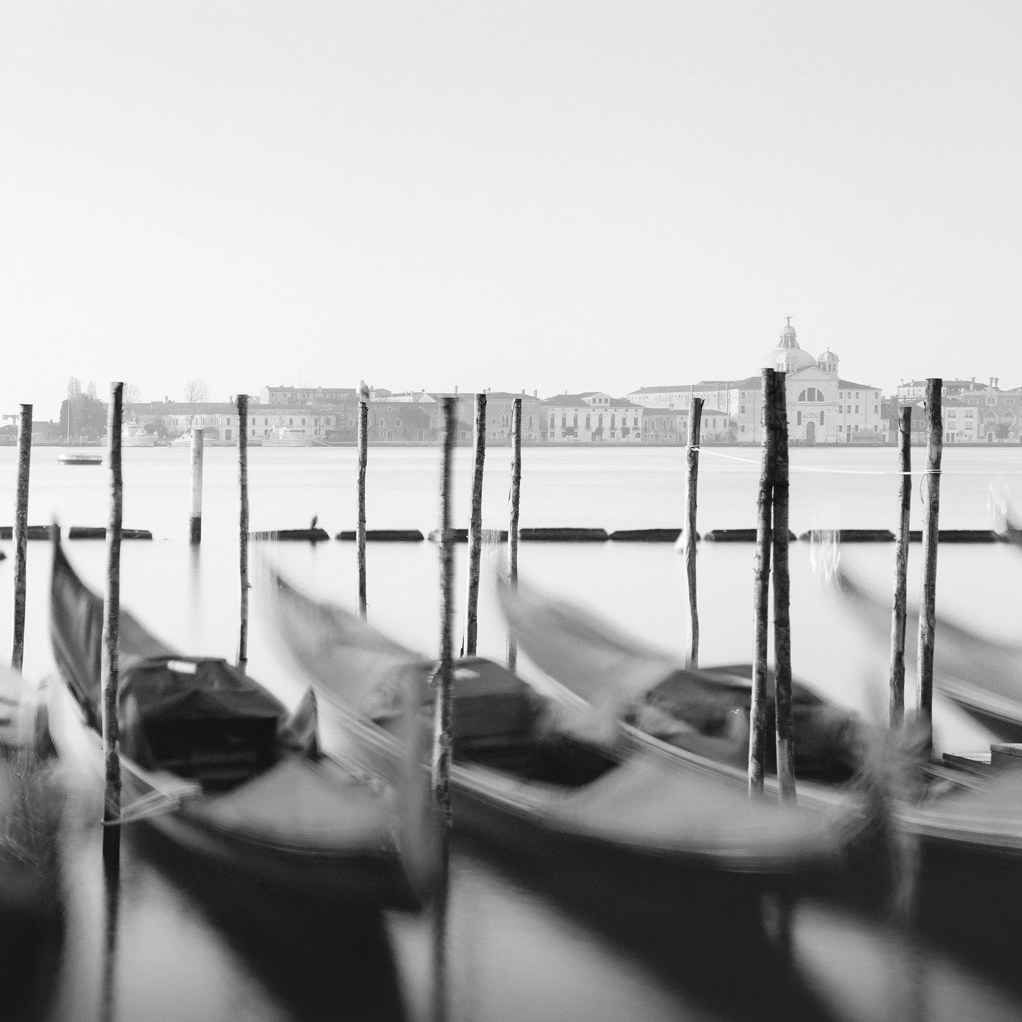 Detail of Twelve Gondolas by Gerald Berghammer showing softly blurred Venetian gondolas, wooden mooring posts and the lagoon.