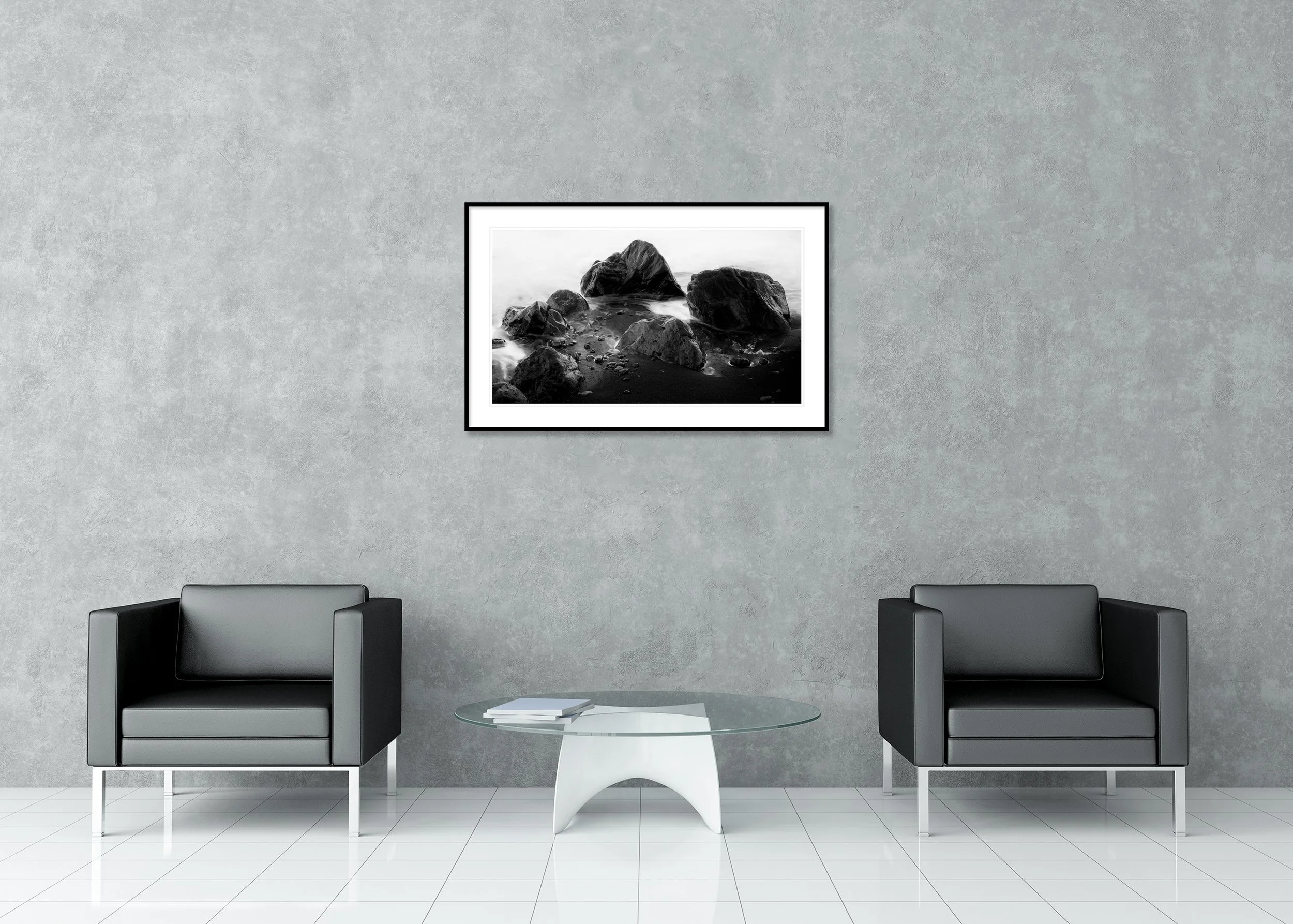Monochrome coastal wall art print with dark shoreline rocks, smooth water and black sand, archival pigment print in a classic frame with a mount