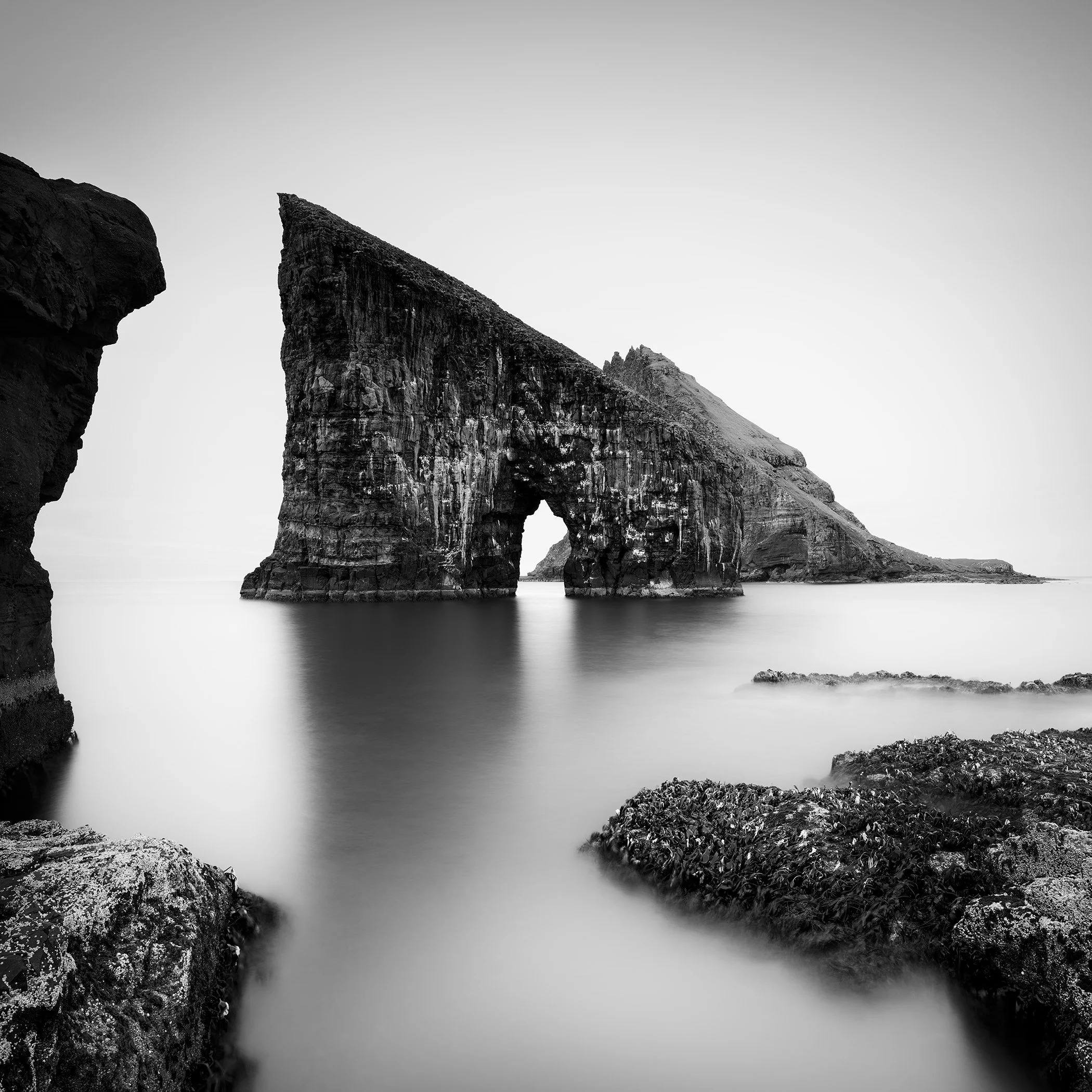 Black and white coastal landscape with a striking sea stack arch and soft long-exposure water