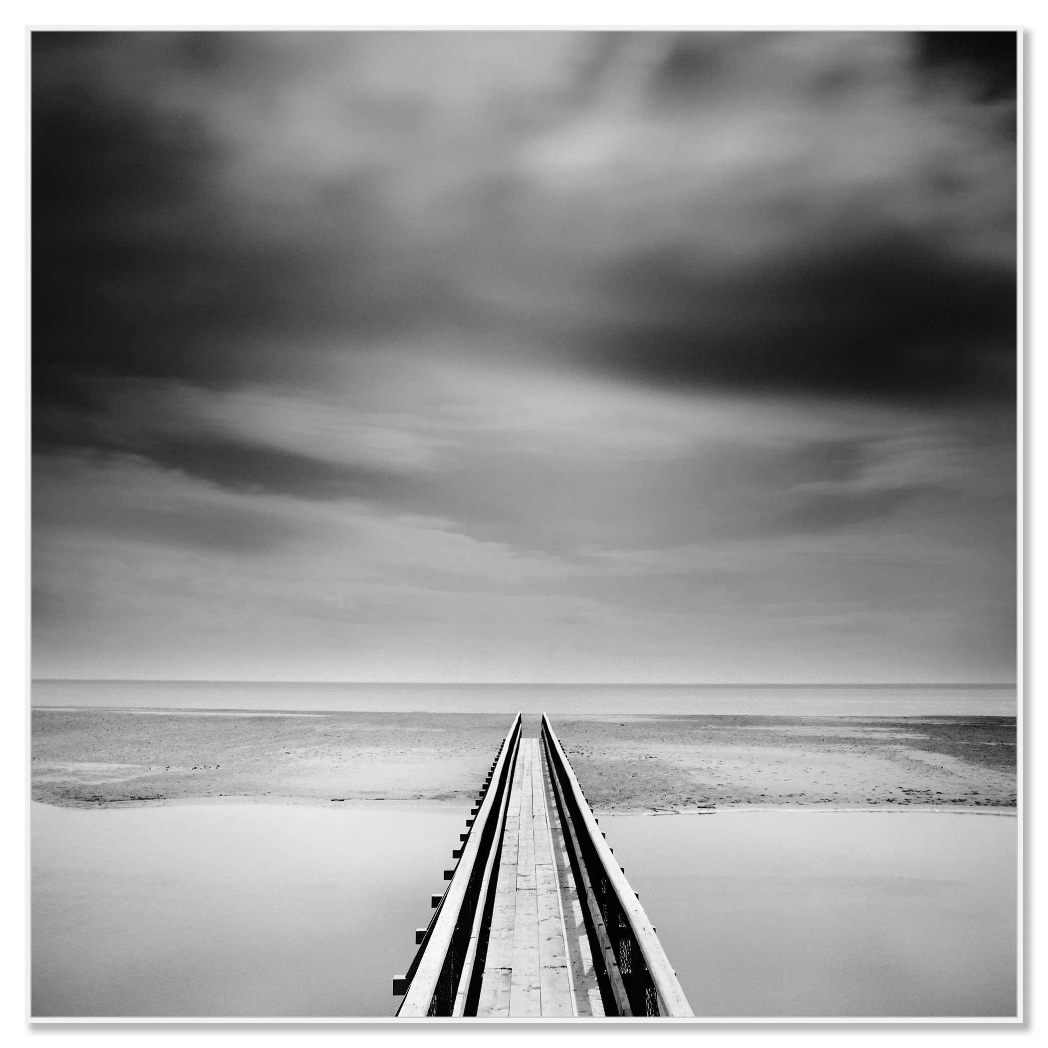 Minimalist monochrome seascape with a narrow pier centred in perspective stretching to the horizon beneath an overcast sky – framed ArtBox white