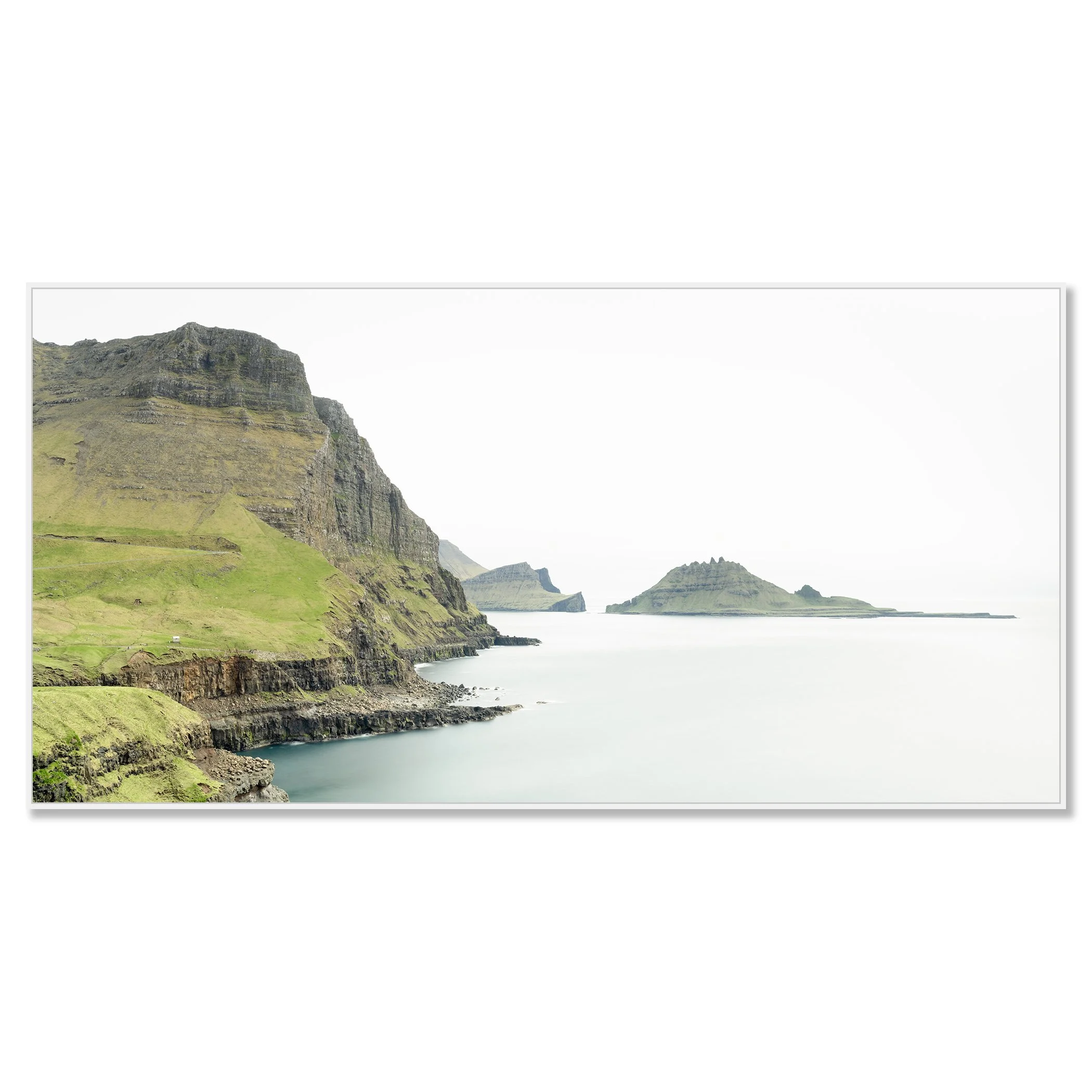 Gerald Berghammer - Color Photography. Cliffs and green hills along a body of water, with distant islands or landmasses in the background under a cloudy sky. Chromaluxe framed white