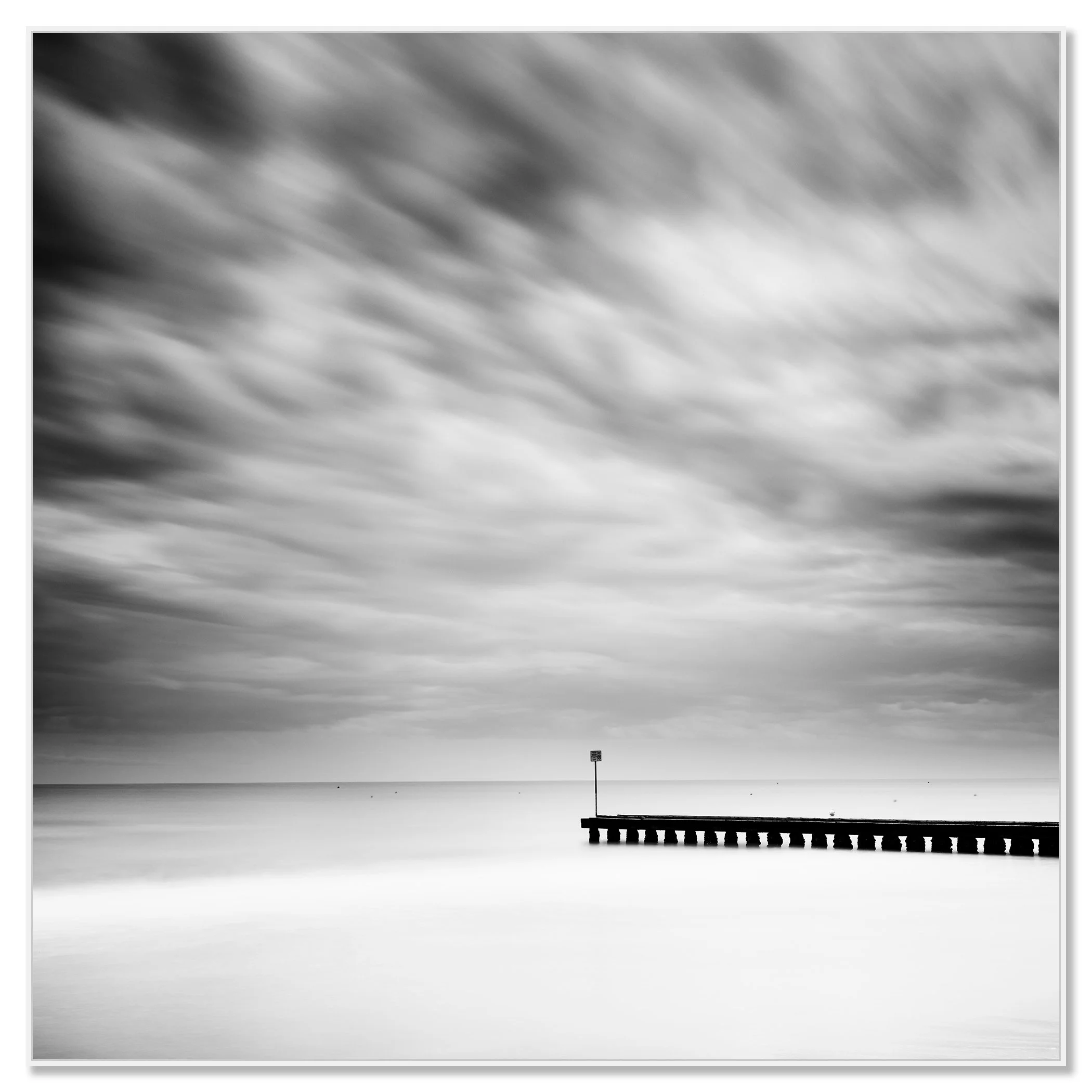 Fine art black and white seascape with moving clouds and a pier reaching towards the horizon – framed ArtBox white
