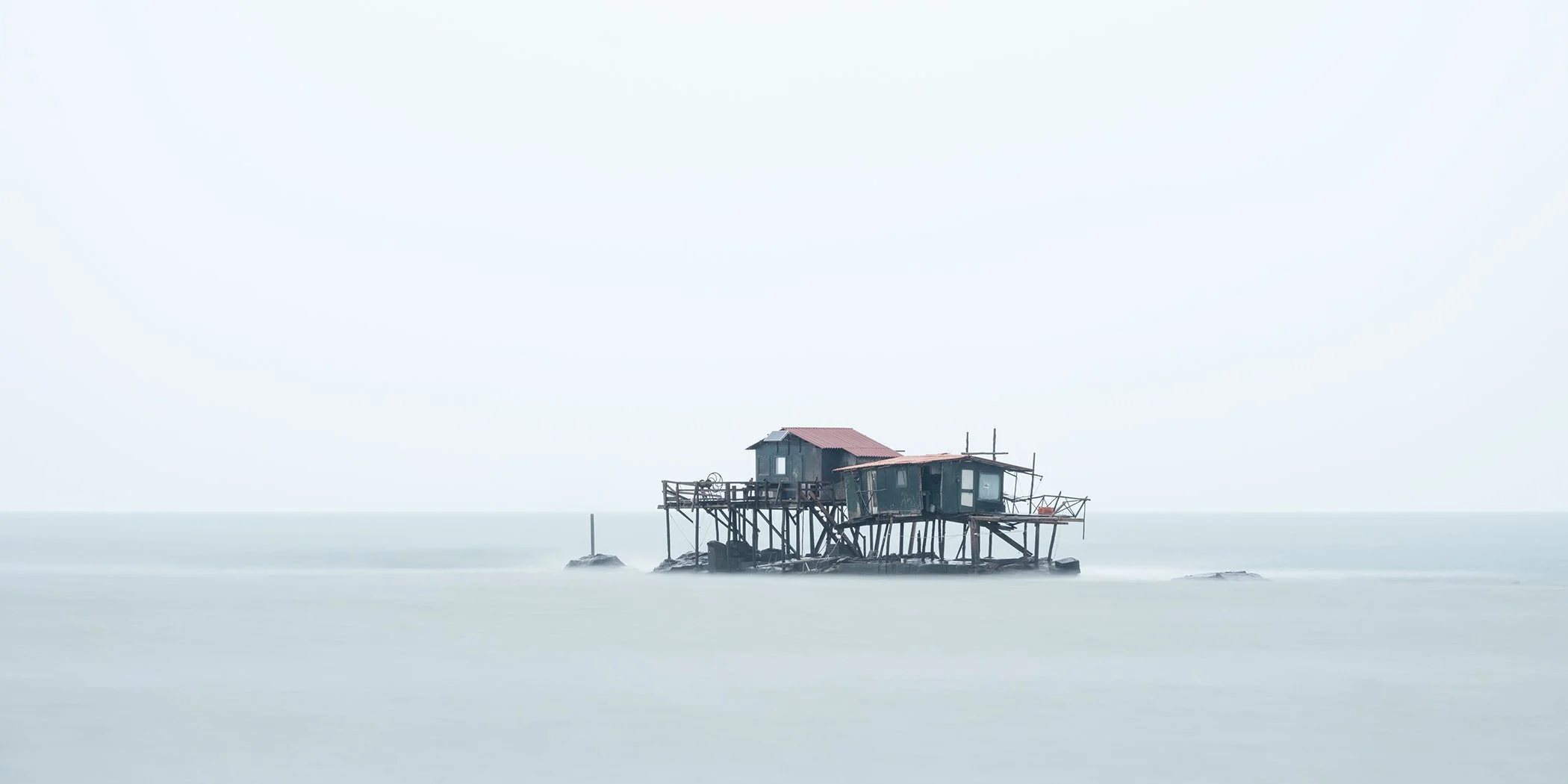 Minimalist colour photograph of a traditional fishing platform above the calm sea in Marina di Pisa, Italy. Photo by Gerald Berghammer.