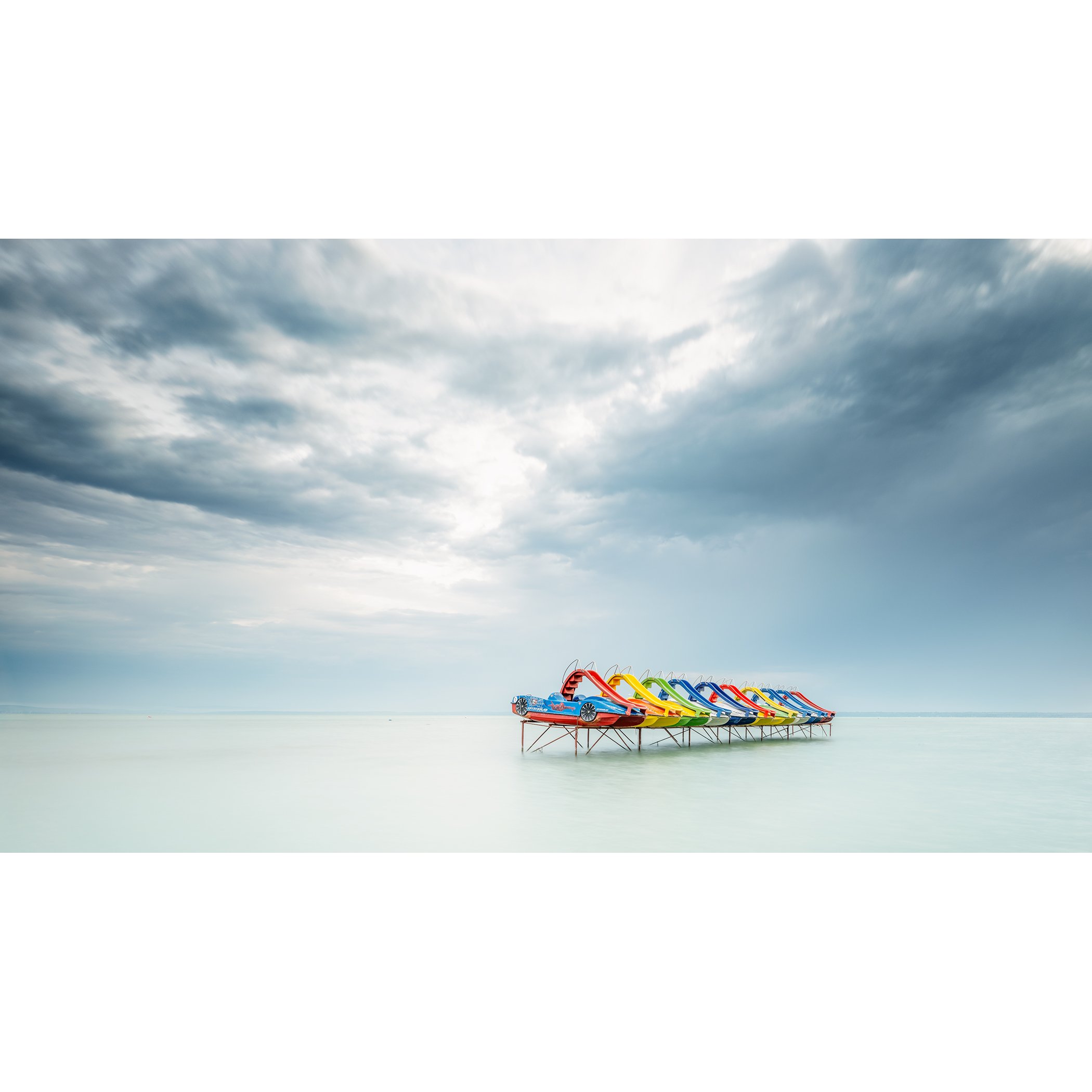 © 2021 Gerald Berghammer - Color panorama waterscape photography. A row of colorful pedal boats on the lake Balaton with dramatic cloudy sky.