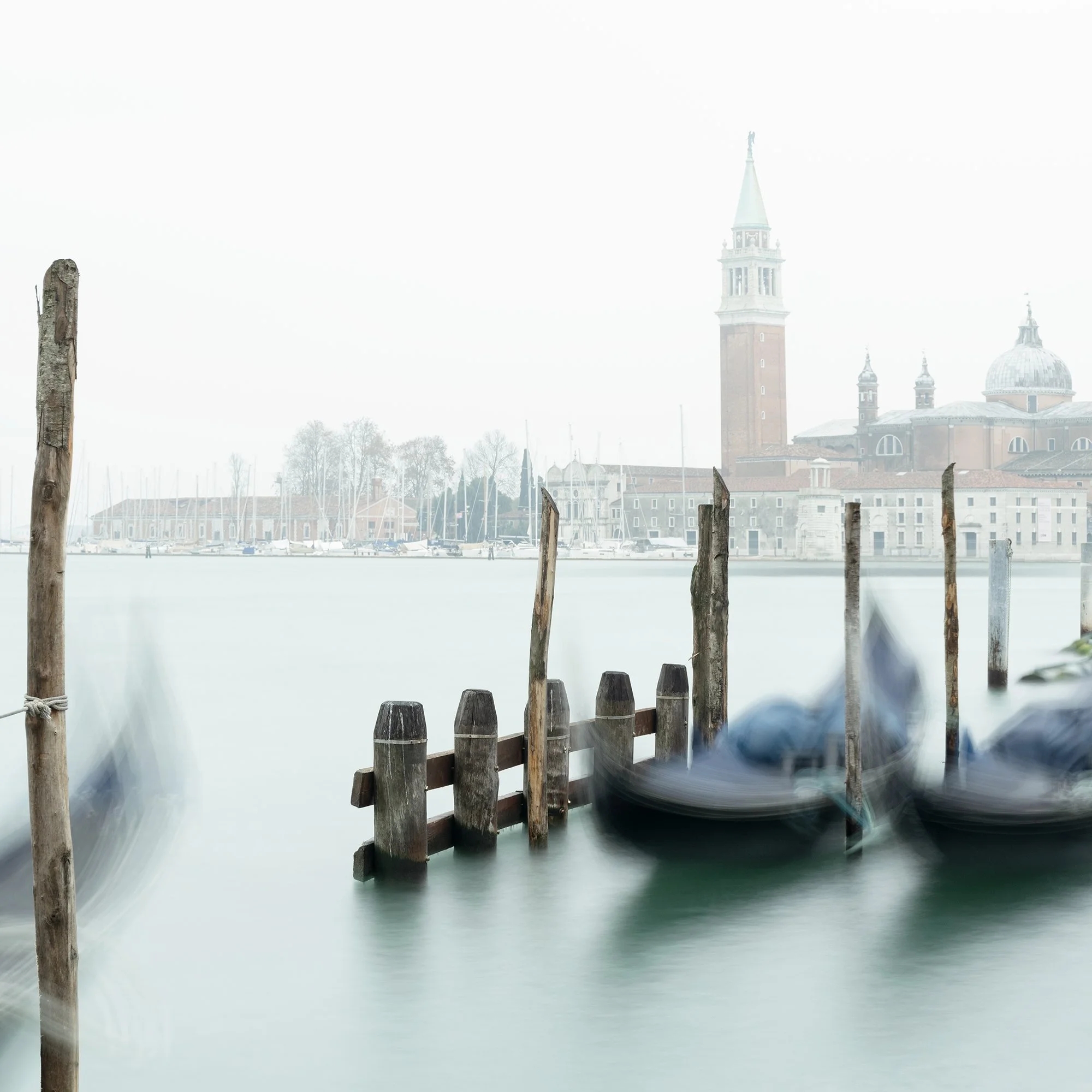 Gerald Berghammer - Color cityscape photography. Gondolas docked along wooden posts on a misty water canal and in back San Giorgio Maggiore Church. Print detail 1