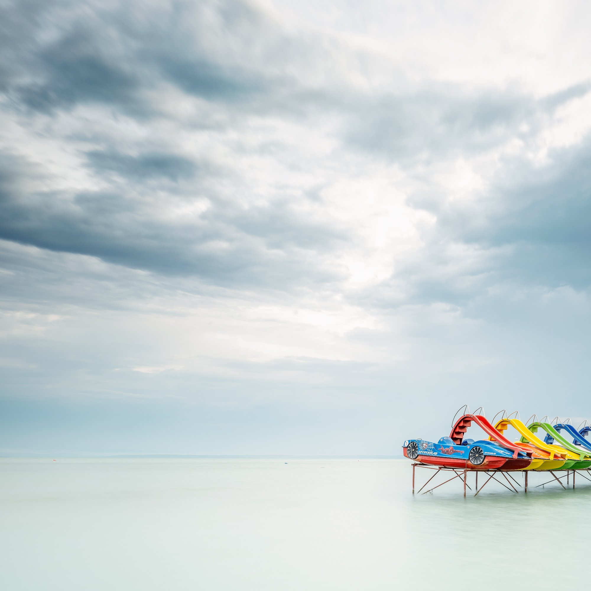 © 2021 Gerald Berghammer - Color panorama waterscape photography. A row of colorful pedal boats on the lake Balaton with dramatic cloudy sky. Print detail 1