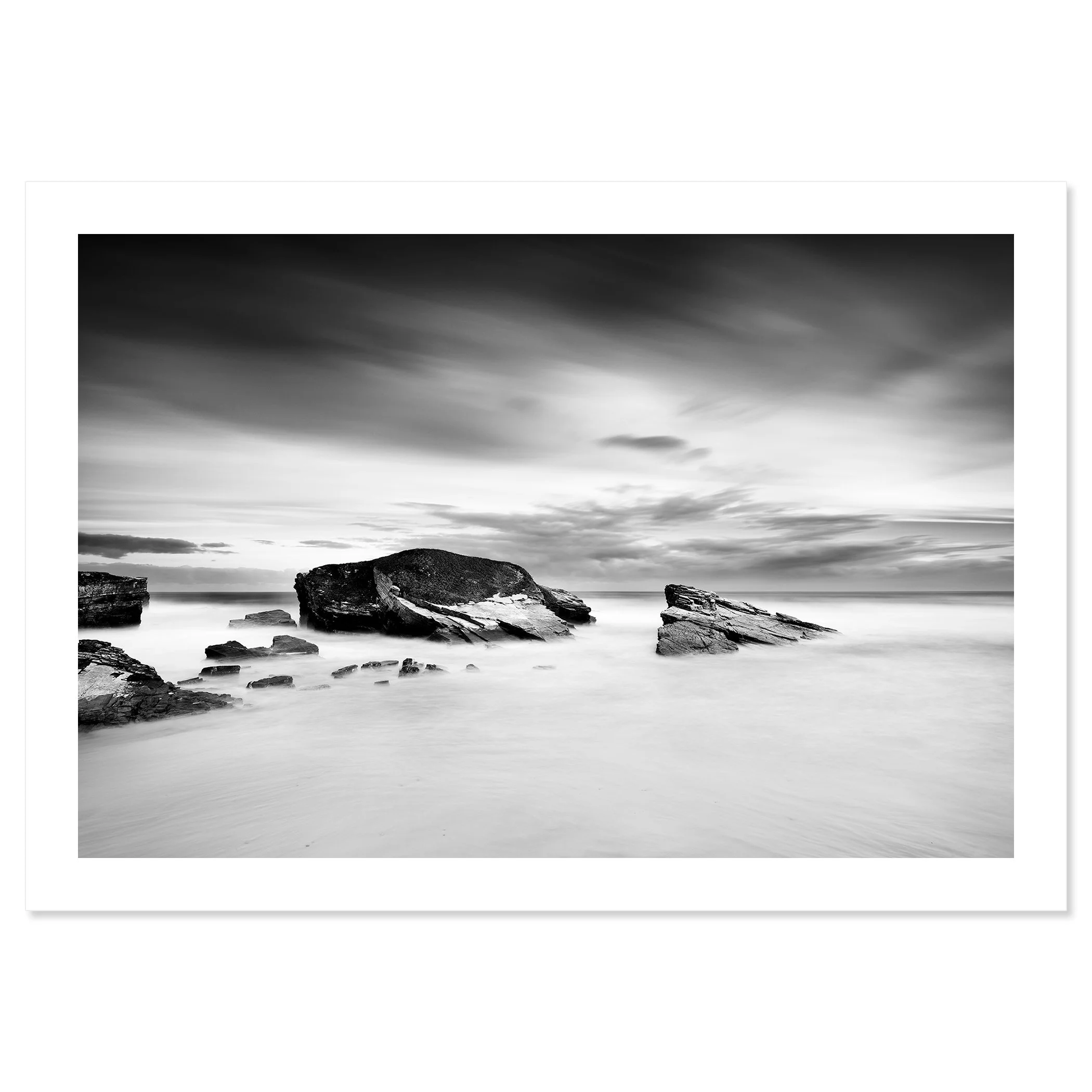 Gerald Berghammer - Black and white long exposure seascape photography. A rocky seashore with large rocks protruding from calm water and a cloudy sky. Fine art print only