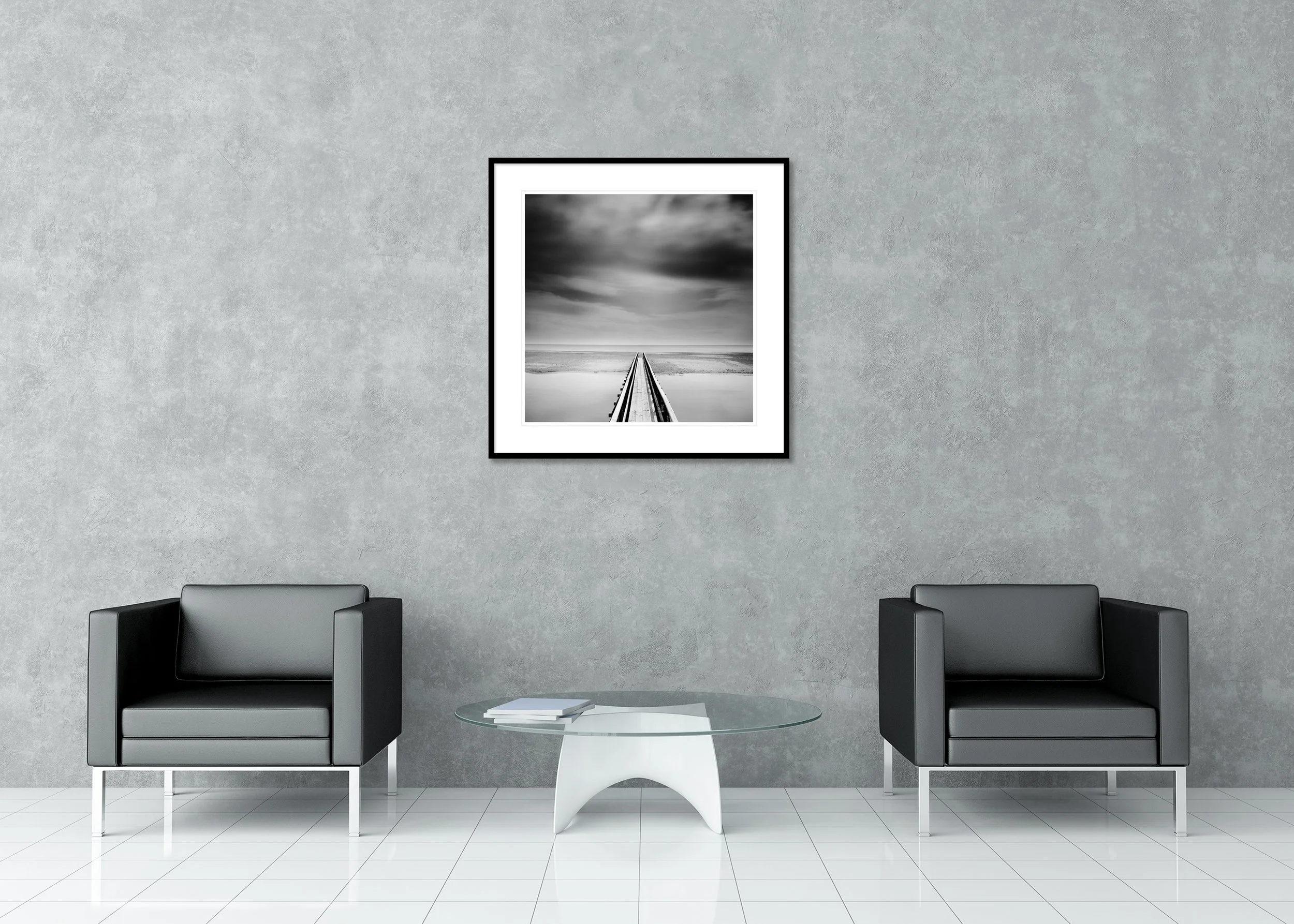 Black-and-white photo of a long wooden pier with a strong vanishing point over still water under moody clouds, archival pigment print in a classic frame with mount.