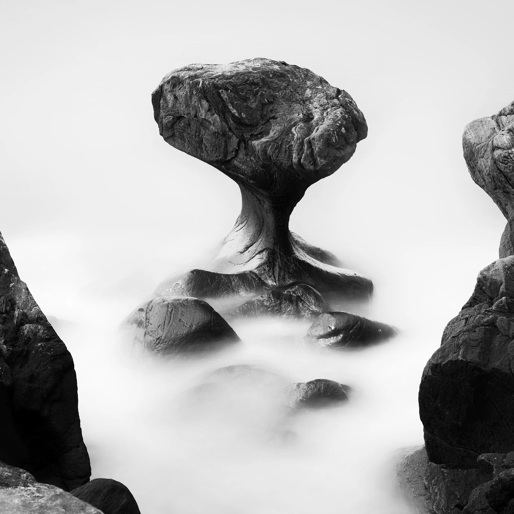 Black and white photo of a mushroom-shaped sea rock rising from misty water