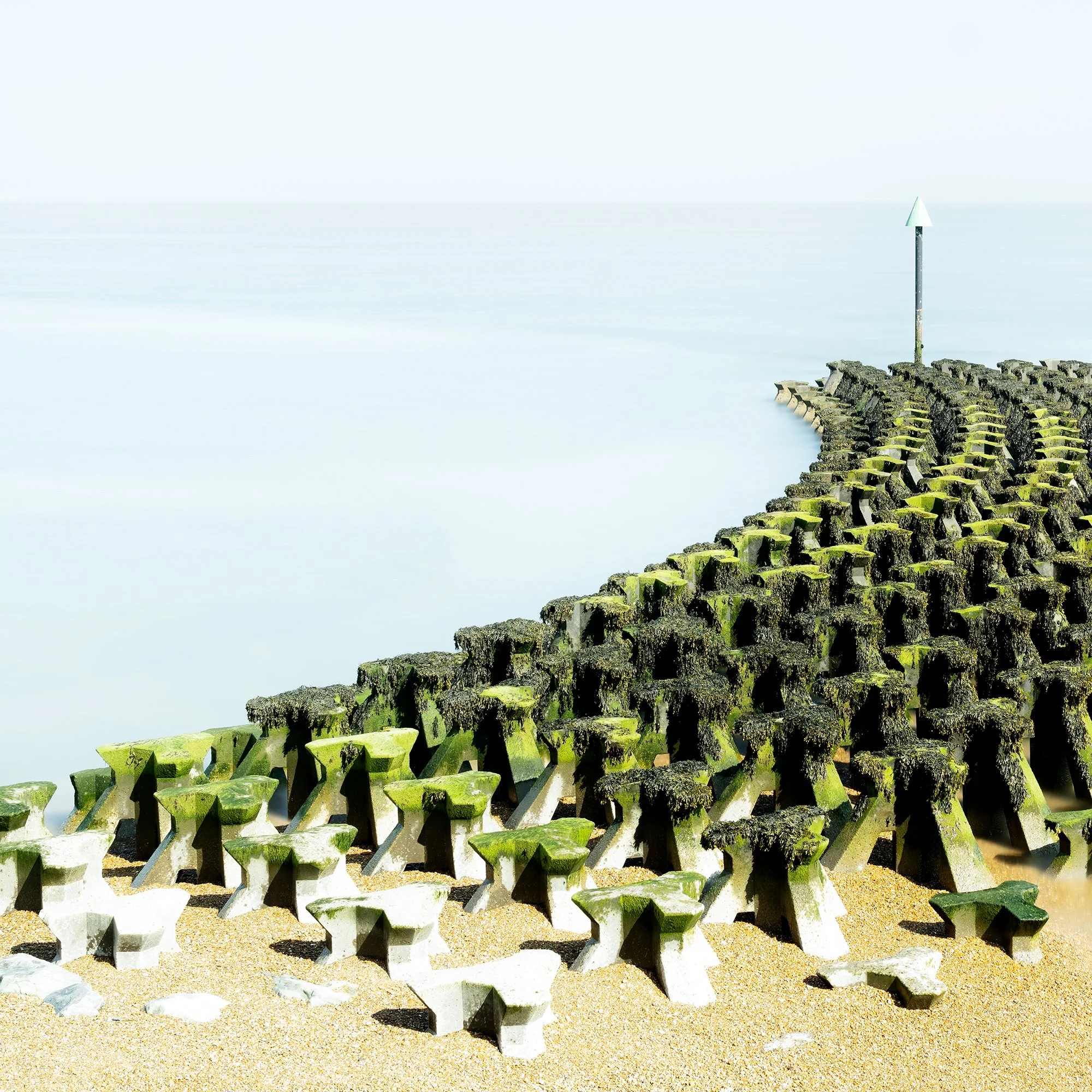 Gerald Berghammer - Color seascape panorama photography. Concrete breakwater structures on a beach extending into the water, with a pole at the end. Print detail 1