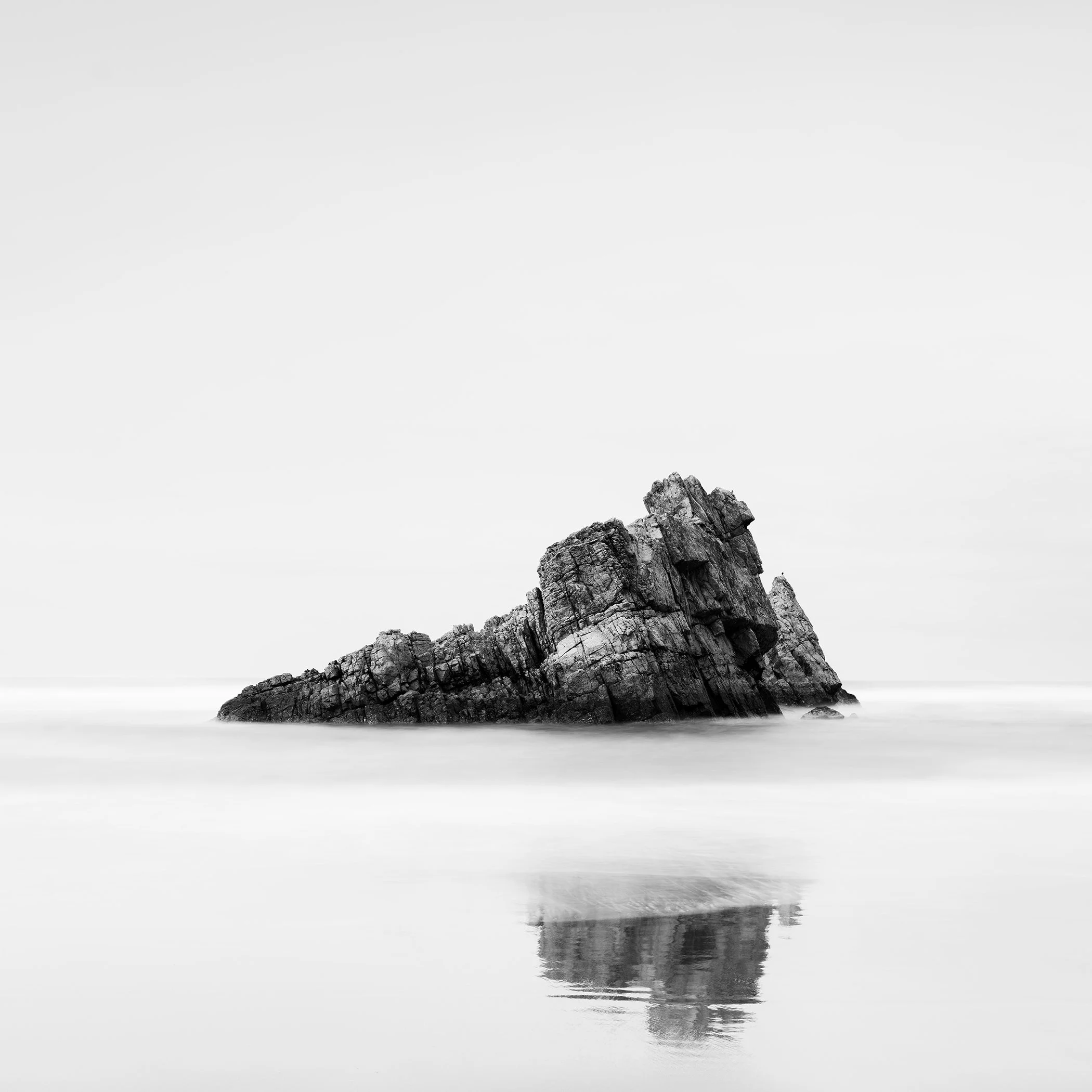 Black-and-white long-exposure photograph of a solitary coastal rock and reflection in Spain, by Gerald Berghammer
