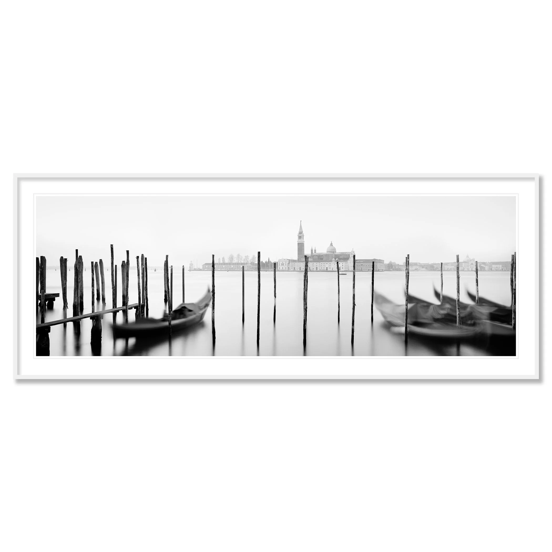 Gerald Berghammer - Black and white cityscape photography. Gondolas moored along wooden posts on a canal with view of a city skyline and a tall bell tower. Classic framed white