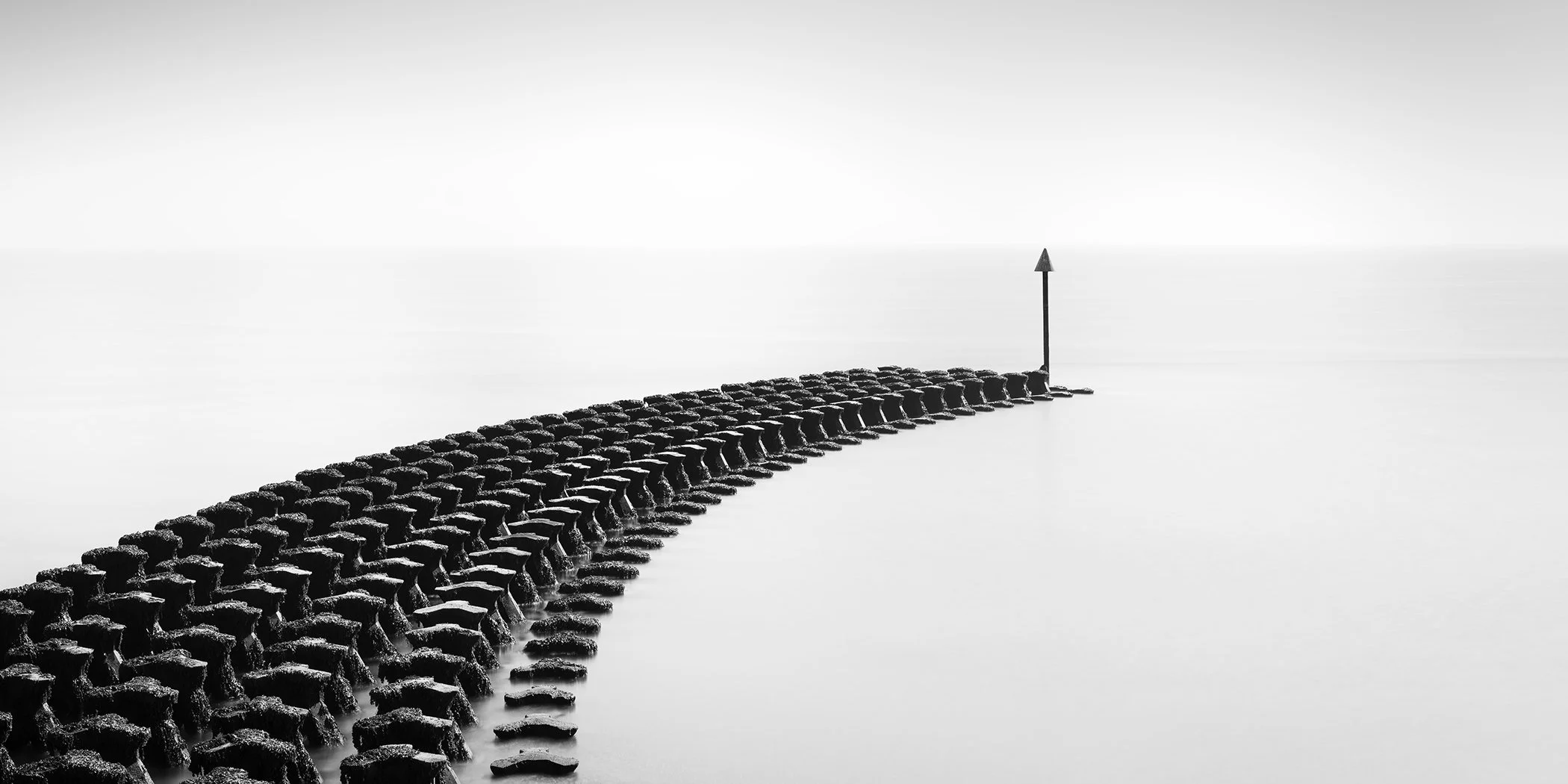 Cobbold’s Point Panorama Study 1 by Gerald Berghammer, minimalist black-and-white seascape of a curved concrete breakwater and navigation marker in Felixstowe, England.