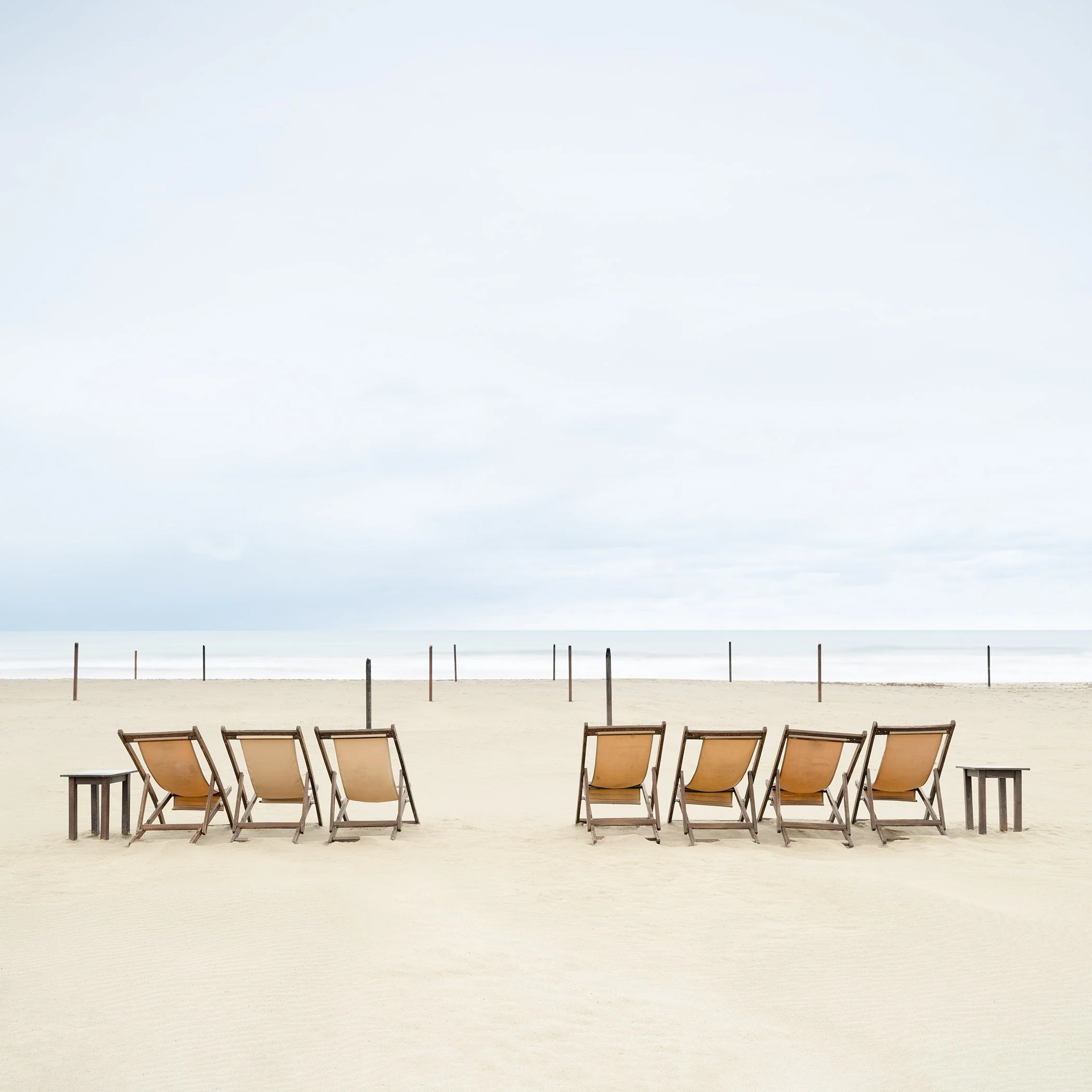 Empty sun loungers beneath a pale blue sky on a quiet Italian beach, photographed by Gerald Berghammer.
