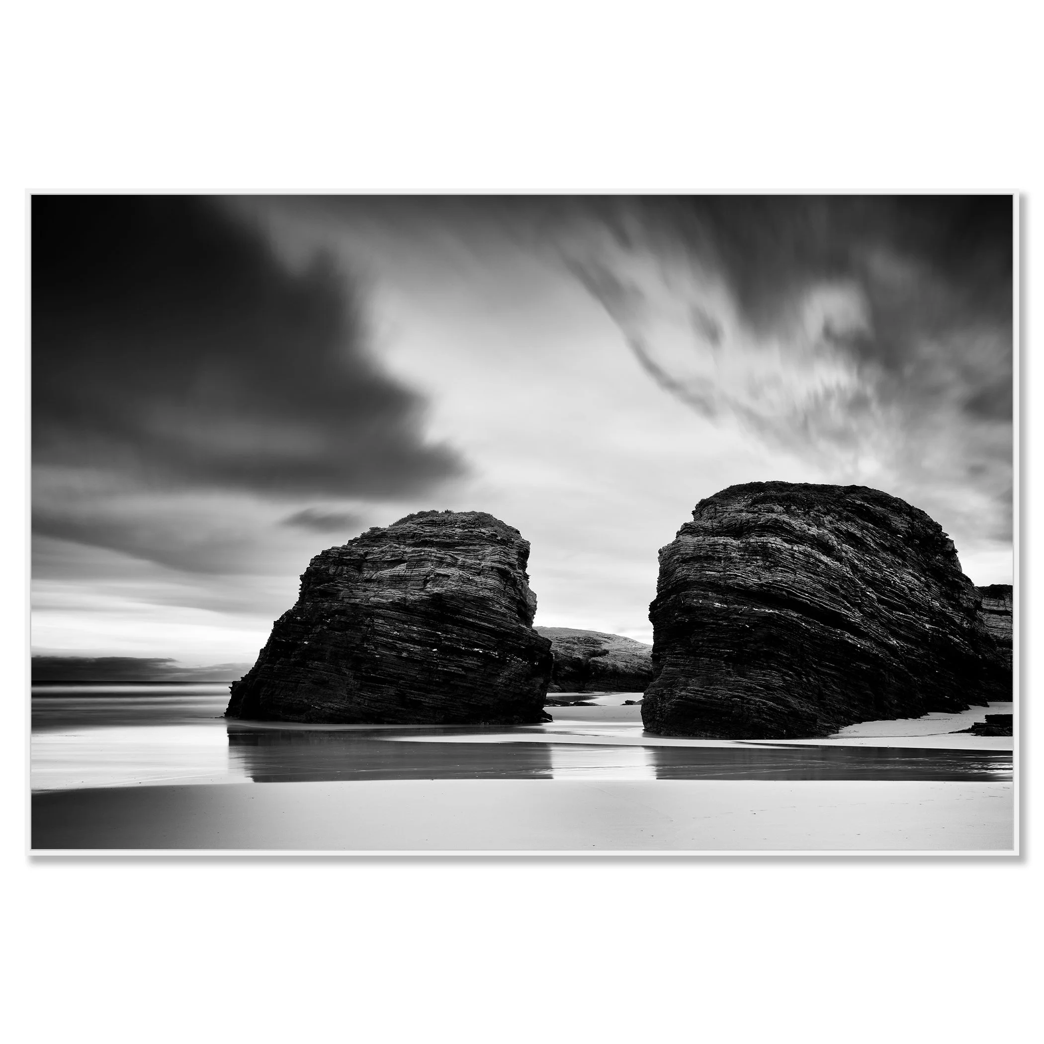 Black and white seascape with two rounded rocks on a beach beneath a cloudy sky – framed ArtBox white