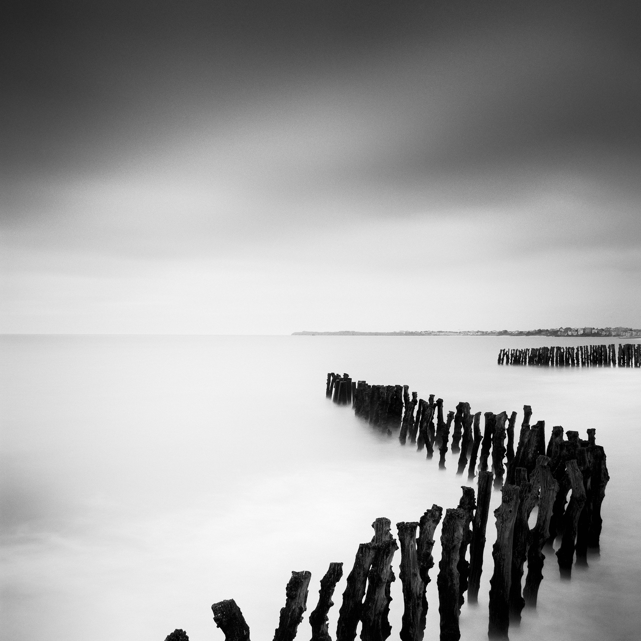 Sea Breakers, France, an analogue black-and-white seascape of wooden groynes beneath a dramatic sky by Gerald Berghammer.