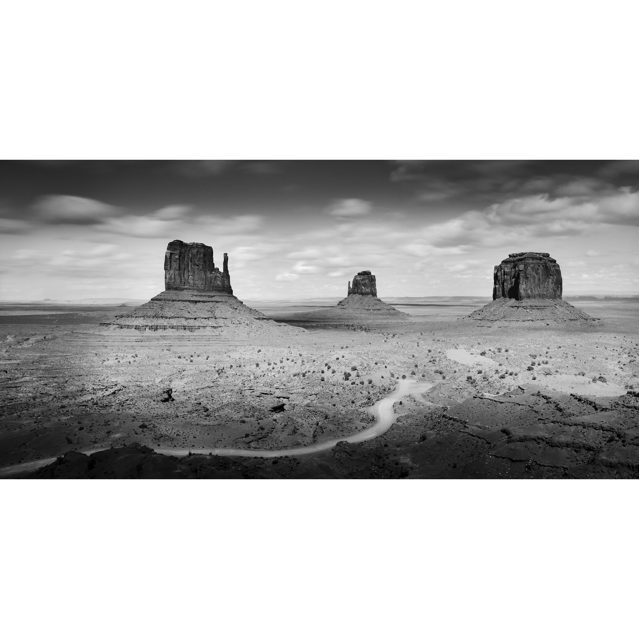 © 2015 Gerald Berghammer - Black and white photo. Large rock formations in a desert landscape, with a winding dirt road in the foreground and a cloudy sky above.