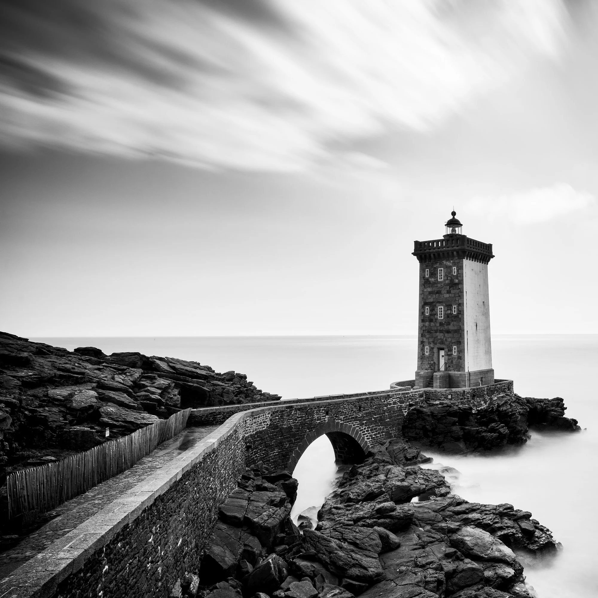 Black-and-white coastal lighthouse with stone bridge across rocks and overcast sky, Detail 1