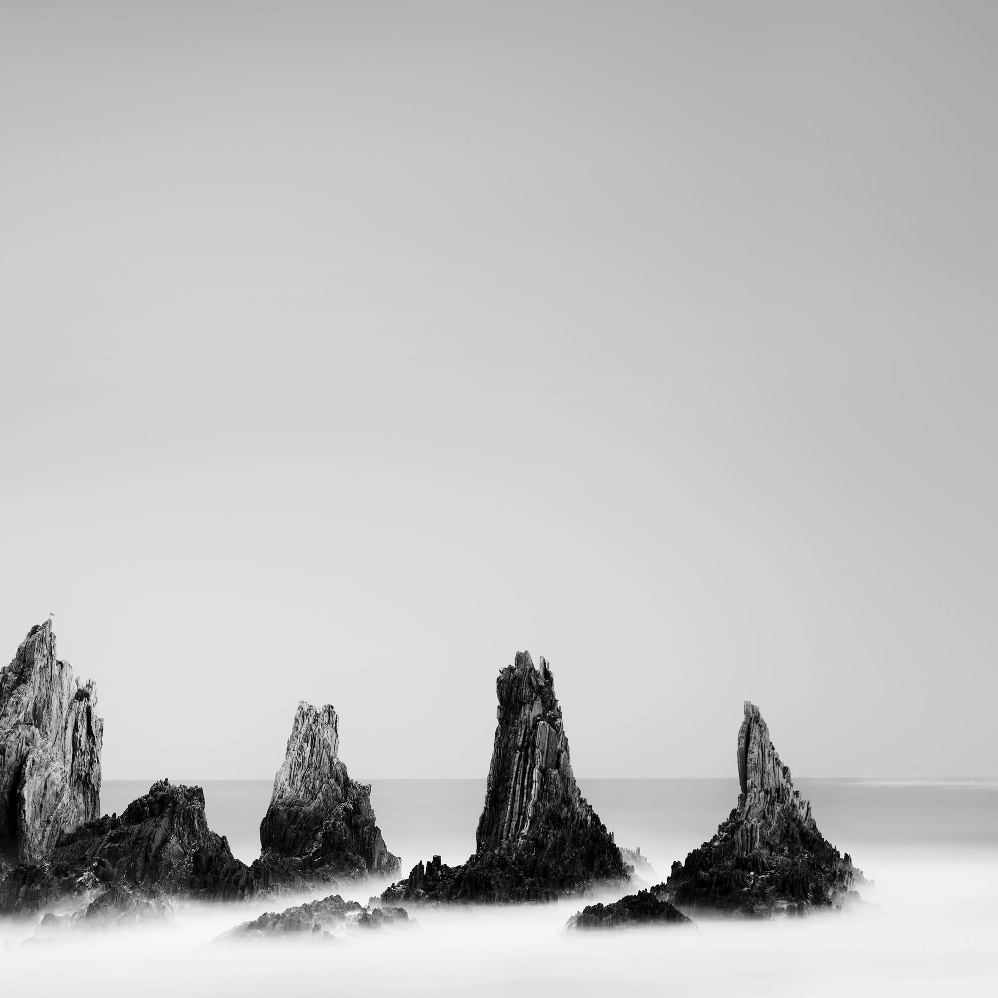 Cropped detail of Rocky Peaks Study 1 by Gerald Berghammer, showing jagged sea stacks rising from the calm Atlantic Ocean in Spain.