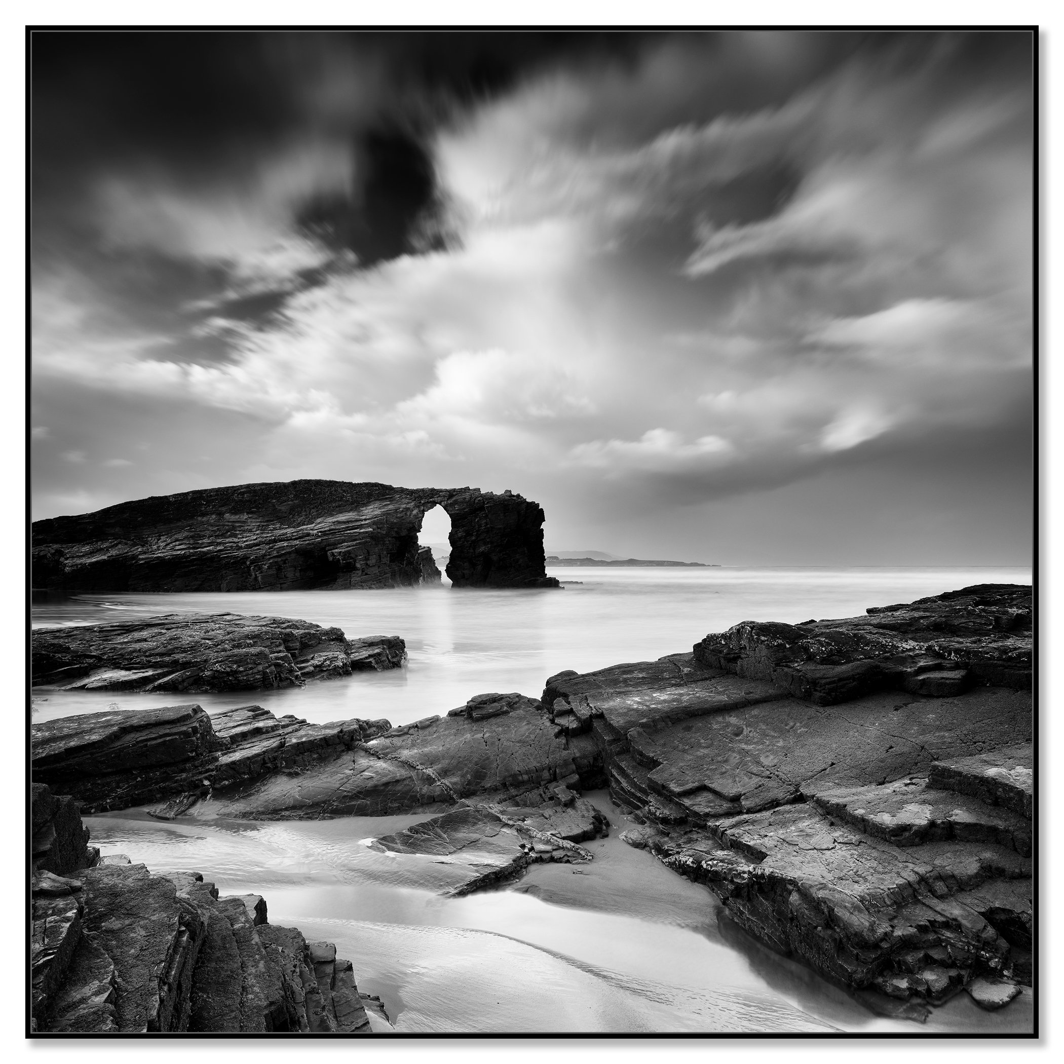 Monochrome seascape featuring layered rocks, a natural sea arch and stormy skies – framed ArtBox black