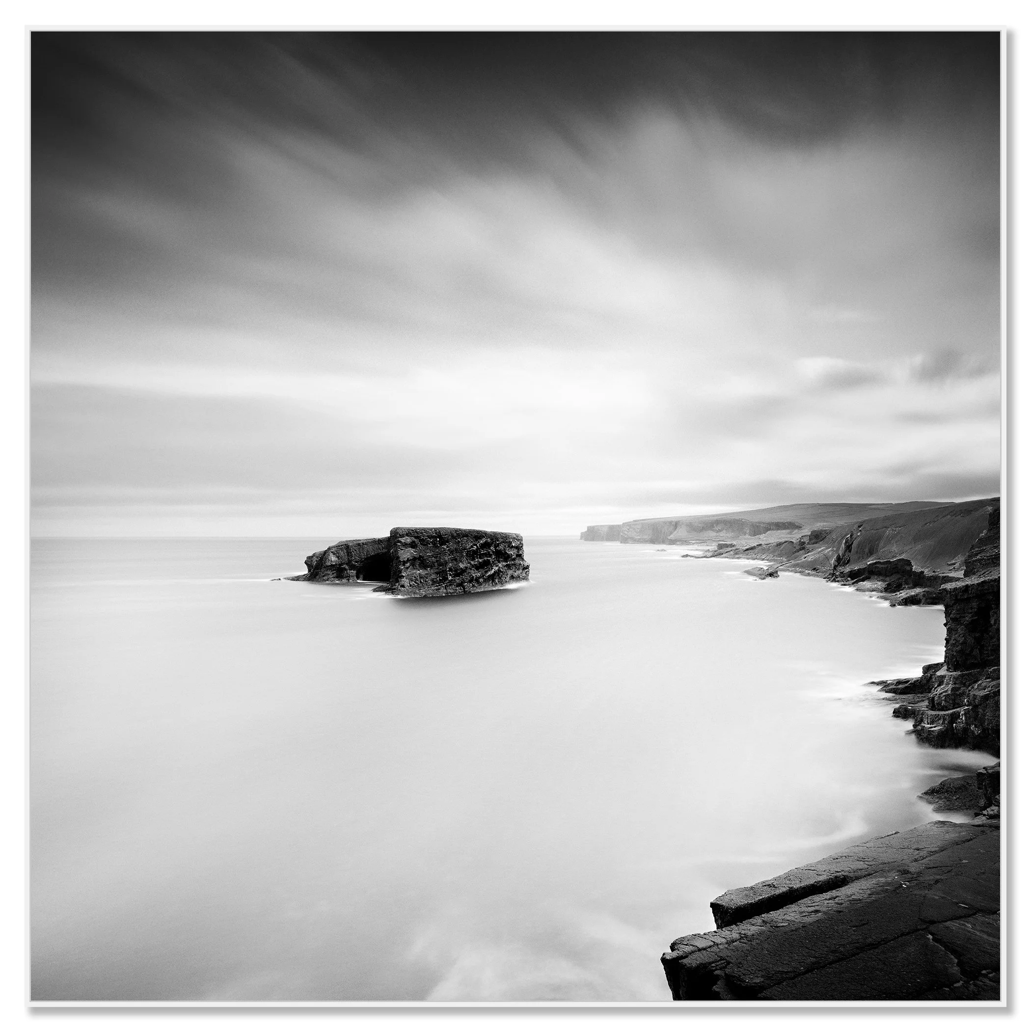 Gerald Berghammer - Black and white long exposure seascape photography. Rocky coastal landscape with cliffs and a large rock formation in the ocean. Chromaluxe framed white