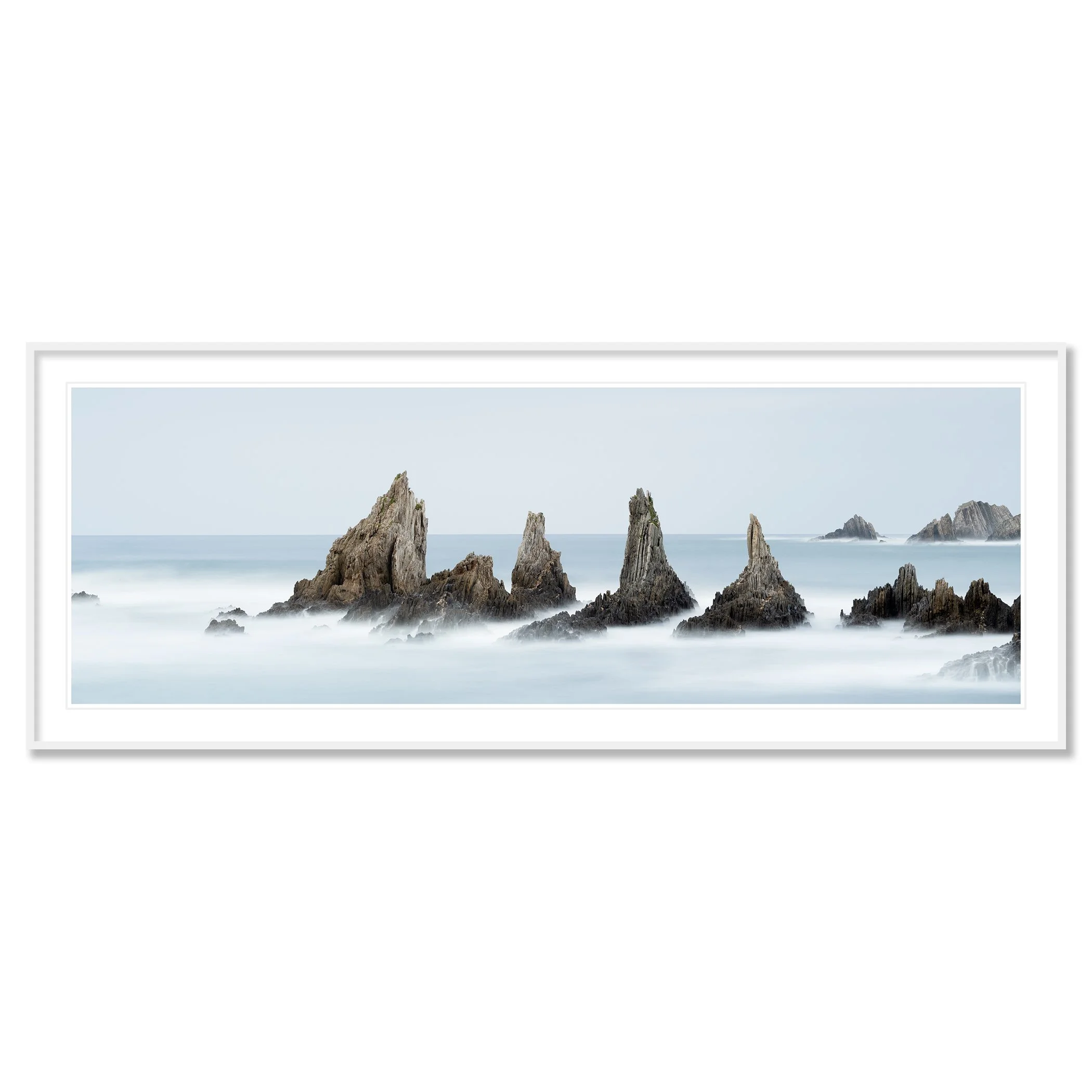 © 2023 Gerald Berghammer - Color seascape. Long exposure photograph of jagged sea stacks rising from the ocean with misty water and a light sky in the background. Classic framed white