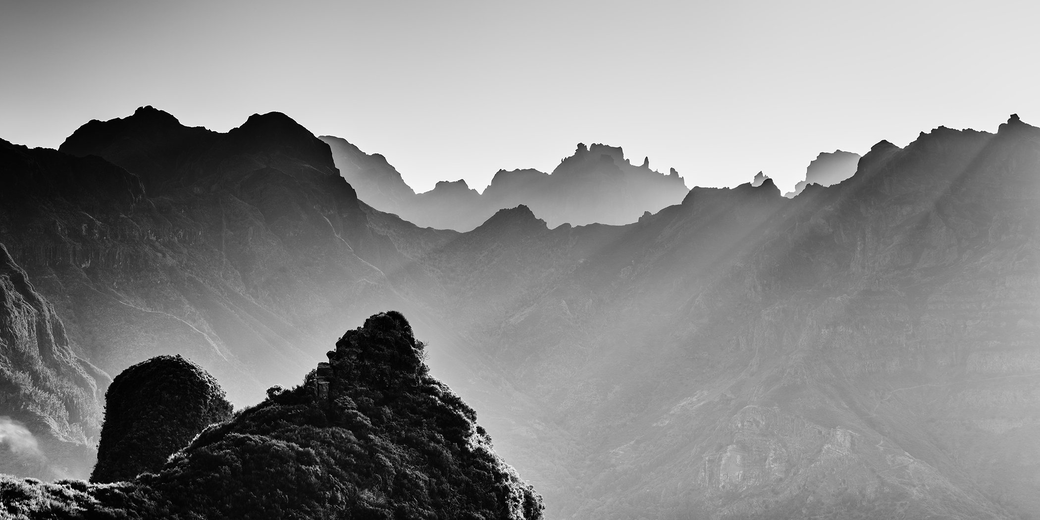 Fine art black-and-white panorama of Madeira’s mountains with rugged peaks, mist and sun rays, by Gerald Berghammer