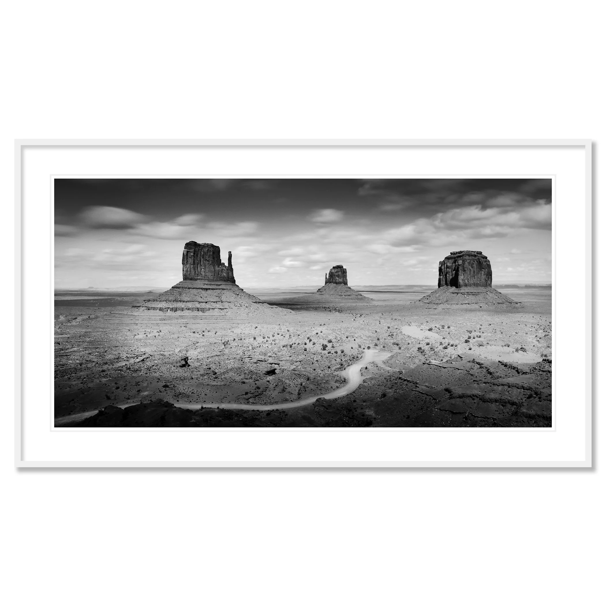 © 2015 Gerald Berghammer - Black and white photo. Large rock formations in a desert landscape, with a winding dirt road in the foreground and a cloudy sky above. Classic framed white