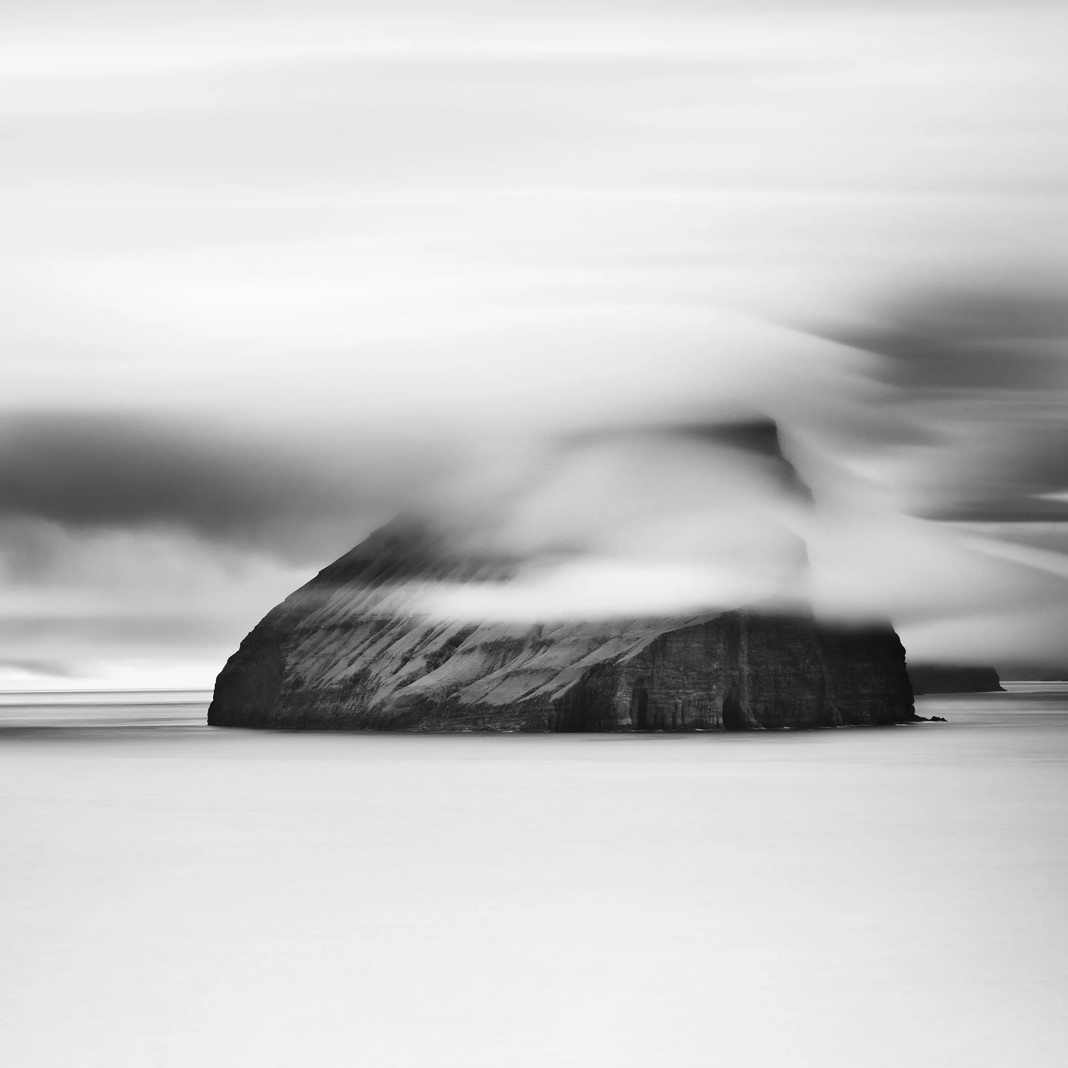 Black and white long exposure of a rocky sea stack surrounded by mist and calm ocean water