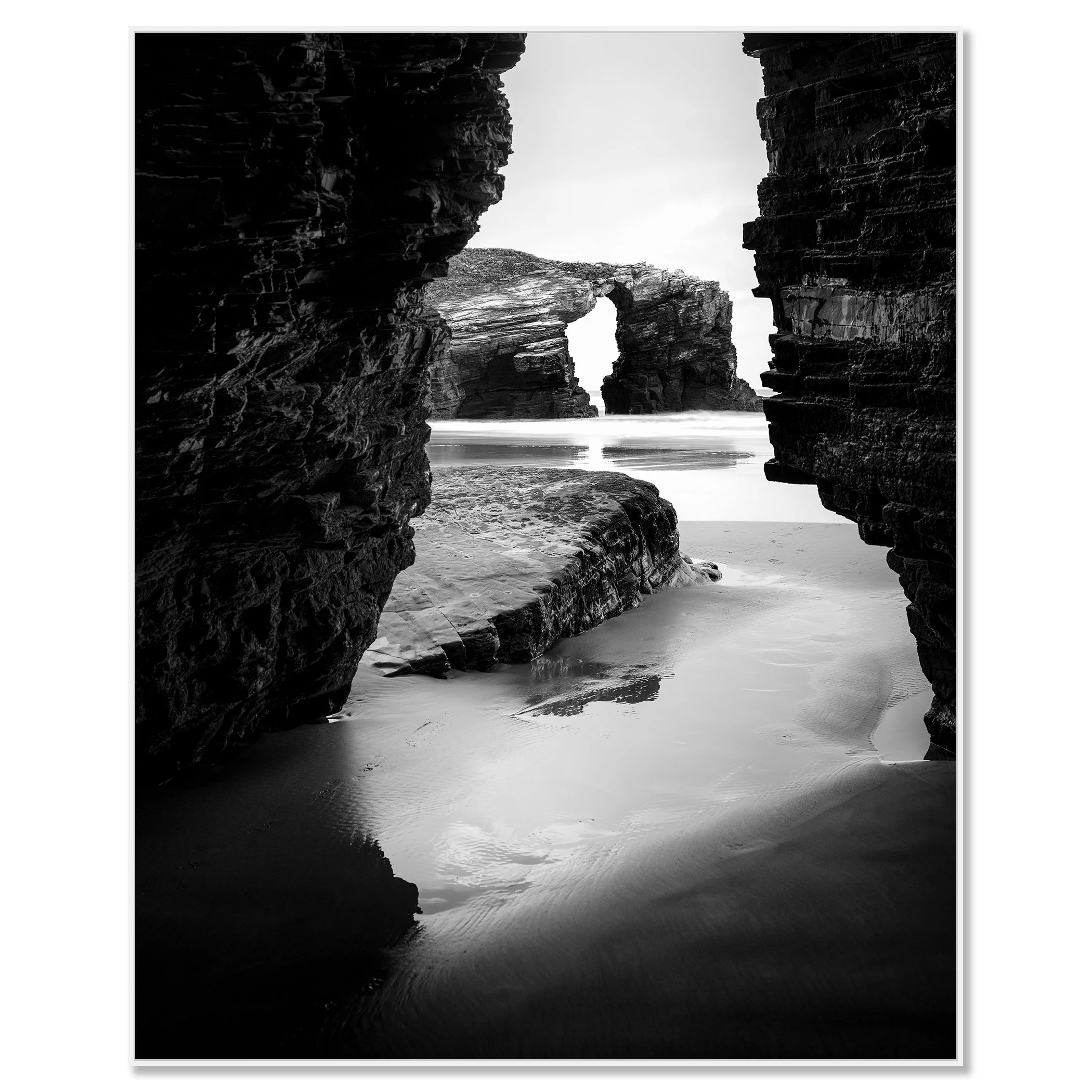 Monochrome seascape photo of Catedrais Beach, Spain, showing a natural rock arch and ocean waves viewed through a narrow opening between large rocks – framed ArtBox white